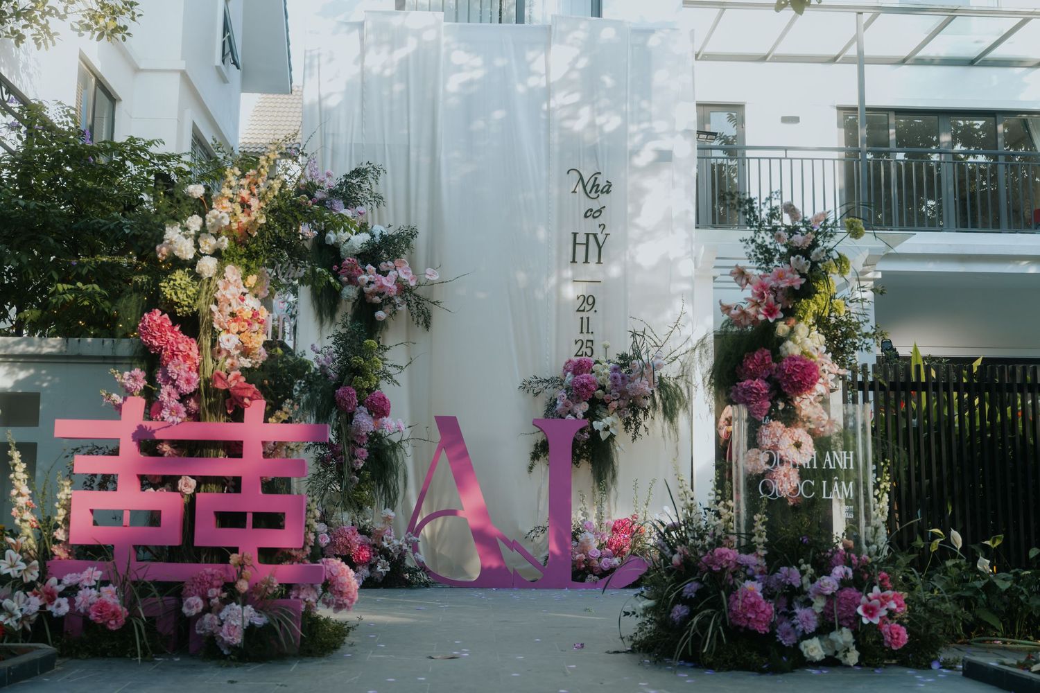 Pink floral wedding entrance decor with double happiness symbol and romantic blooms at an outdoor Vietnamese wedding ceremony.
