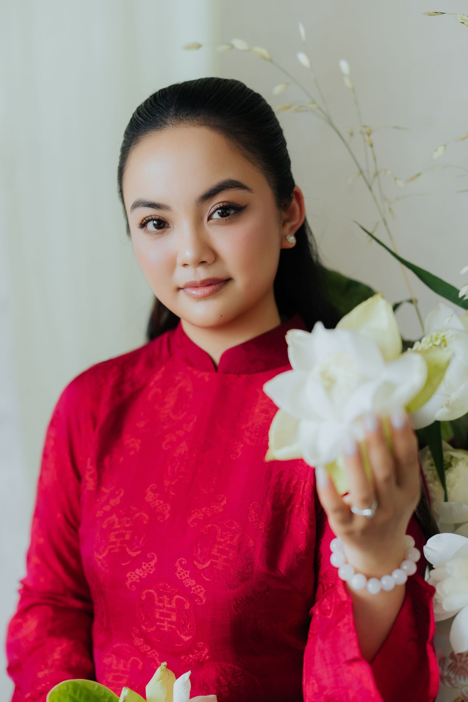 Young Vietnamese woman in red ao dai holding white lotus flowers, posing elegantly for a portrait photo.