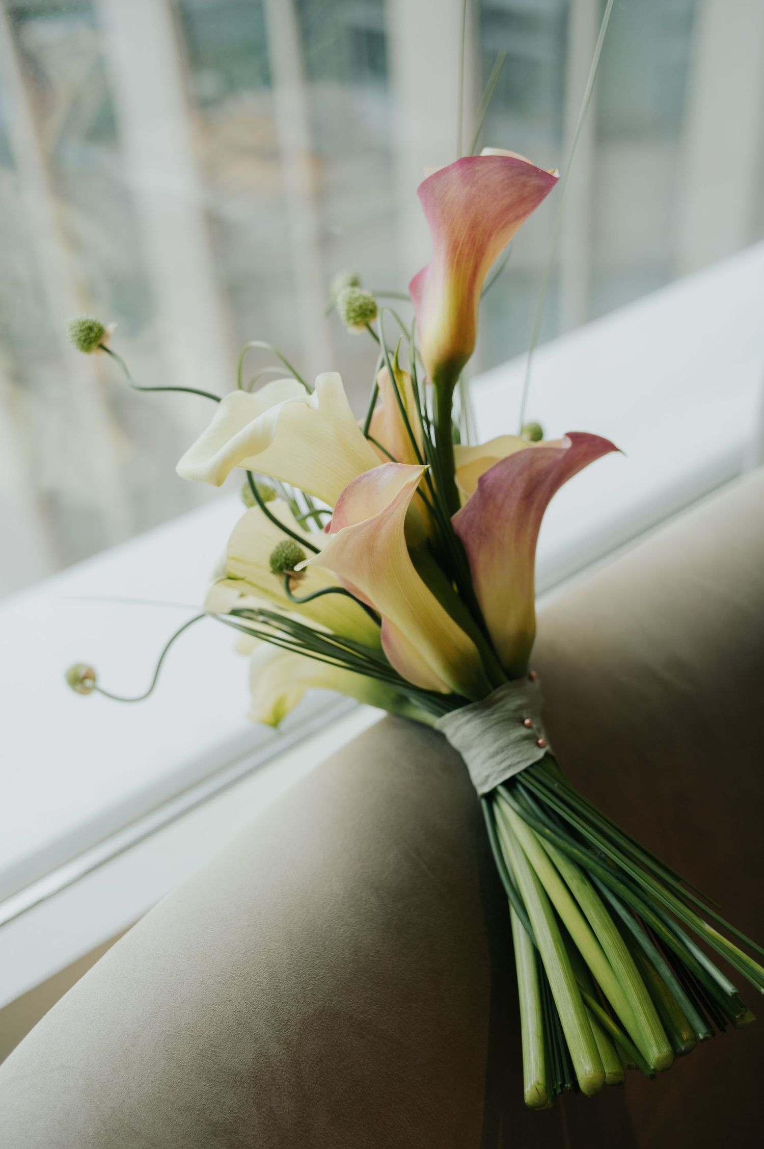 Elegant bridal bouquet of pink and white calla lilies resting on a windowsill in soft light.