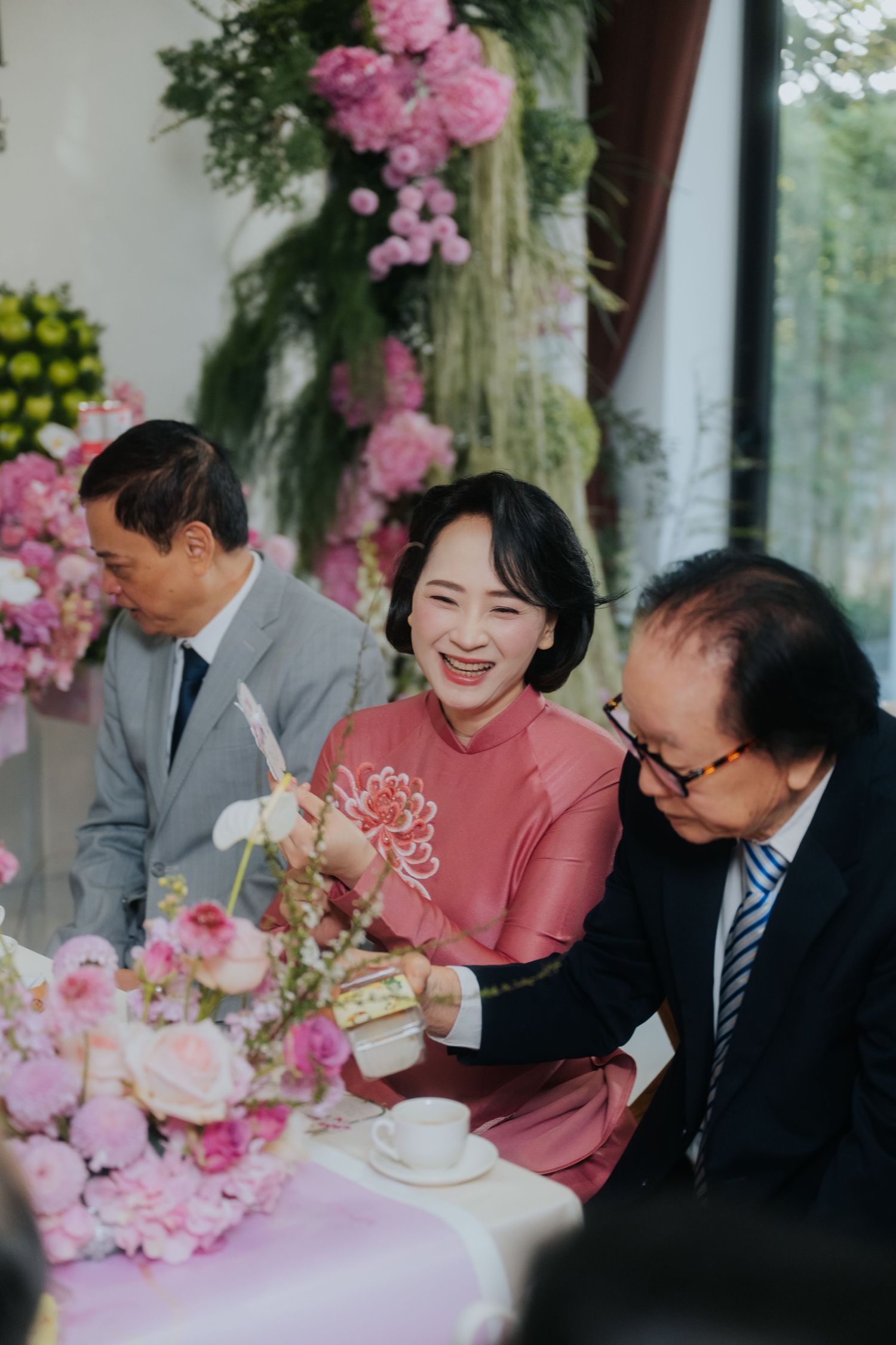 Elegant Asian wedding reception with guests in pink ao dai and suits seated at floral table with pink roses and peonies.