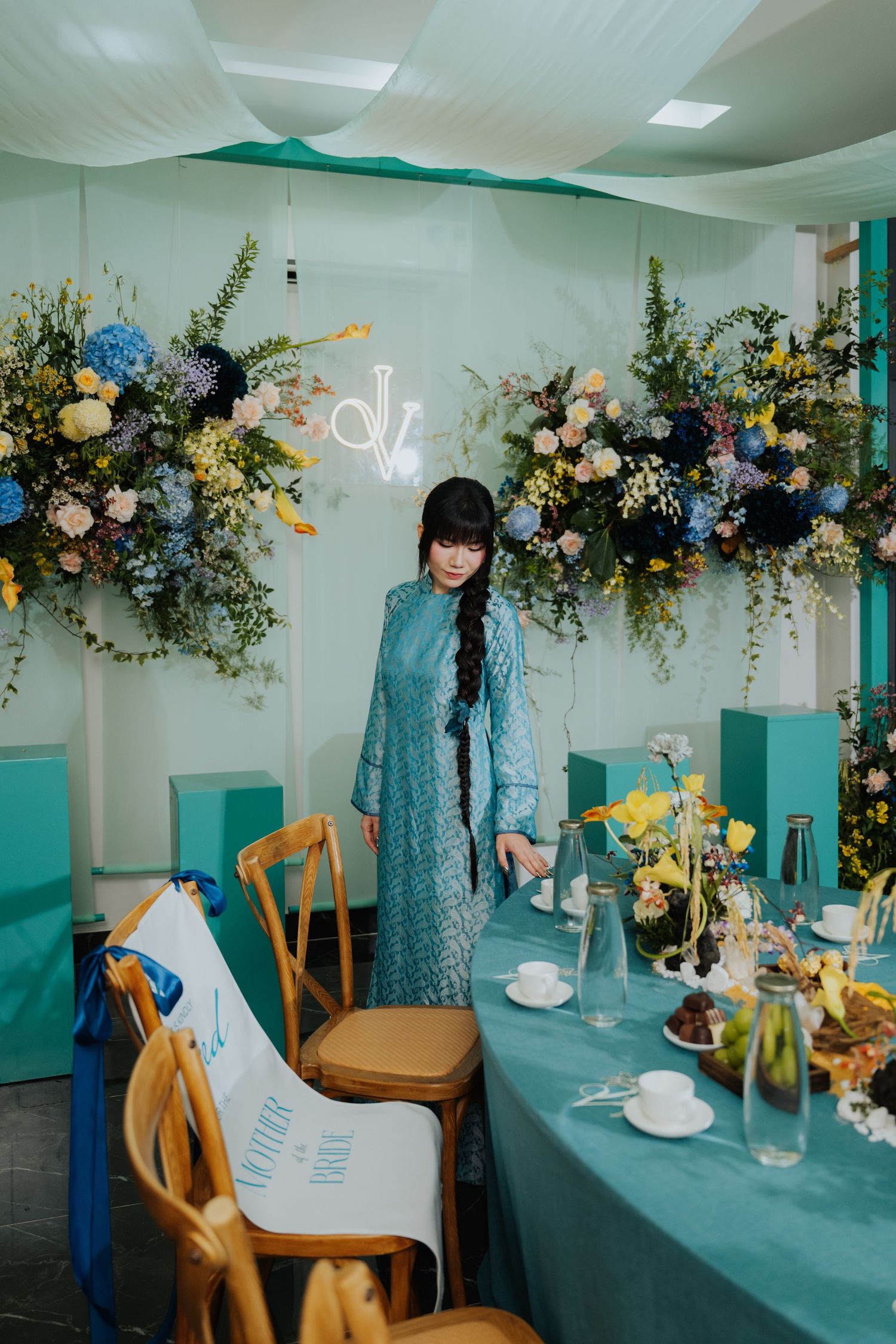 Woman in teal dress arranging a decorated table with floral arrangements in a mint-themed wedding reception venue.
