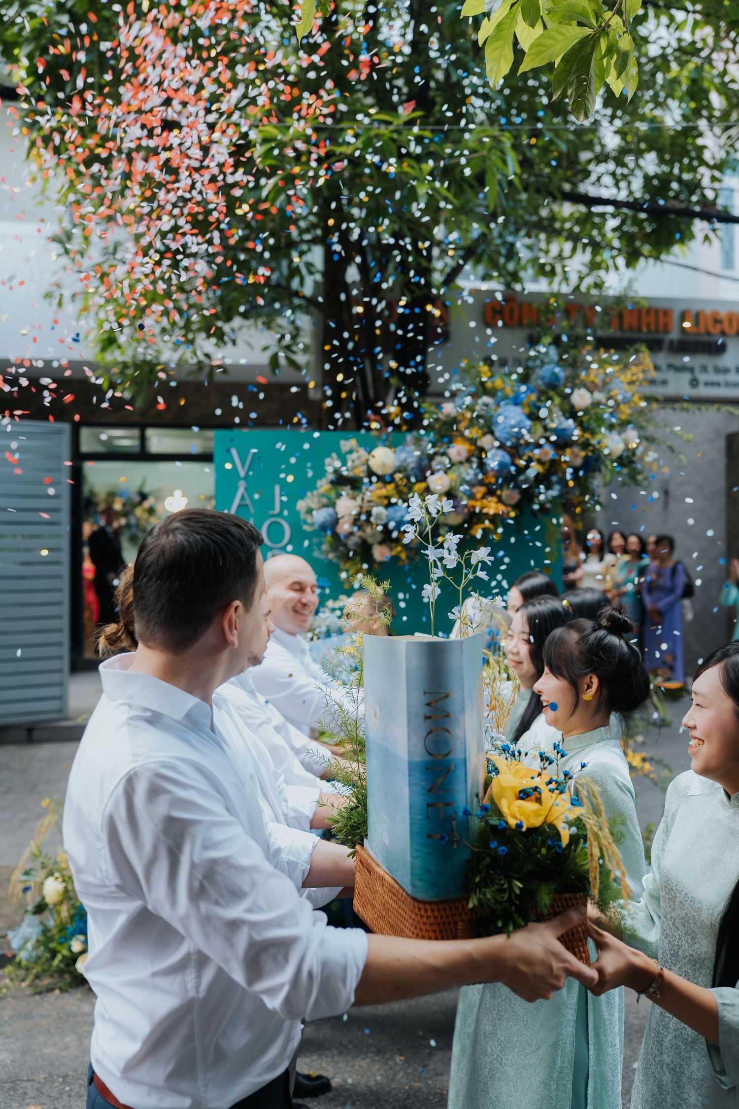 Joyful wedding celebration with confetti falling as couple holds floral arrangement outdoors in Vietnam.