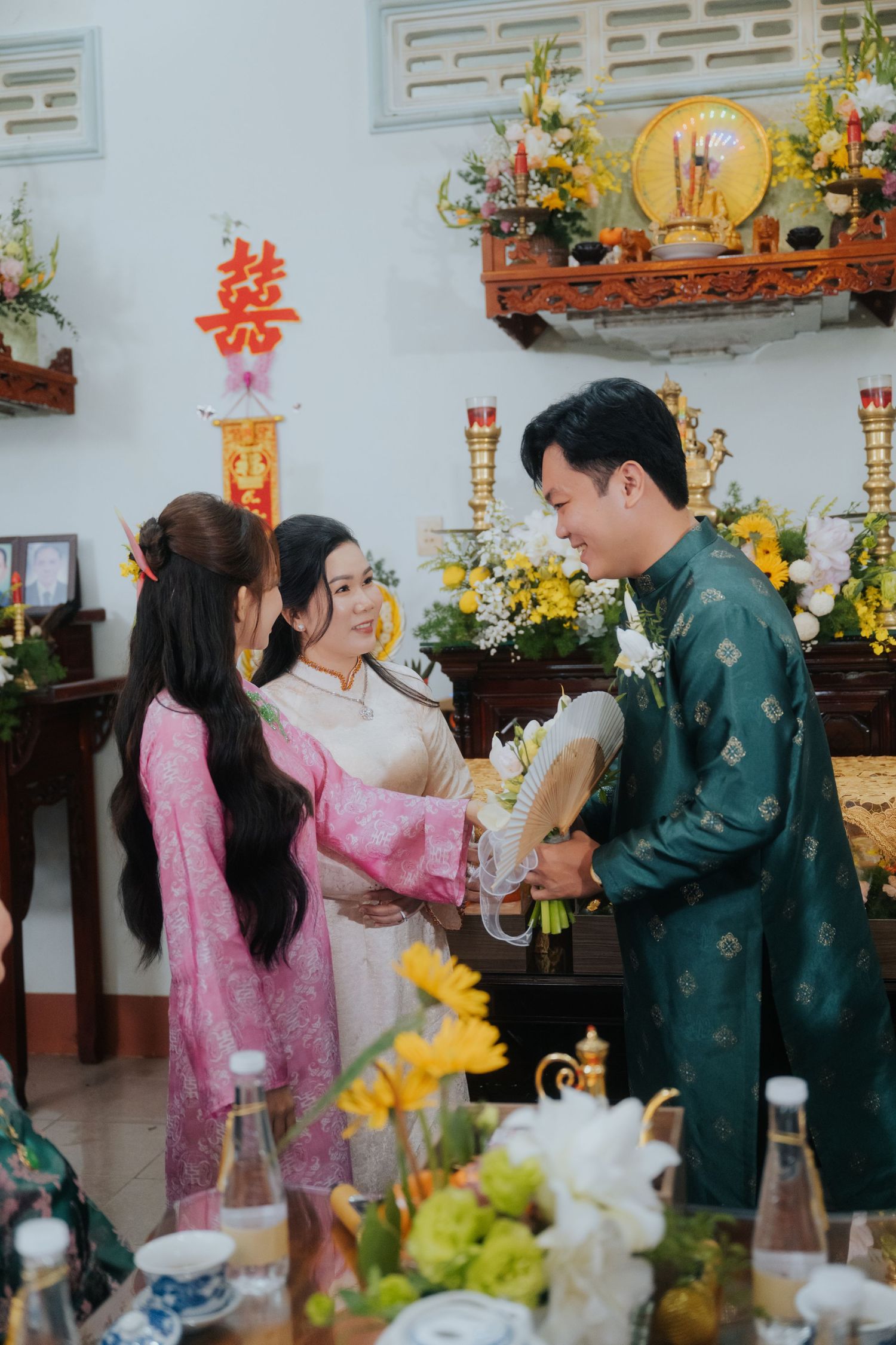 Vietnamese traditional wedding ceremony with couple in ao dai exchanging flowers at family altar.