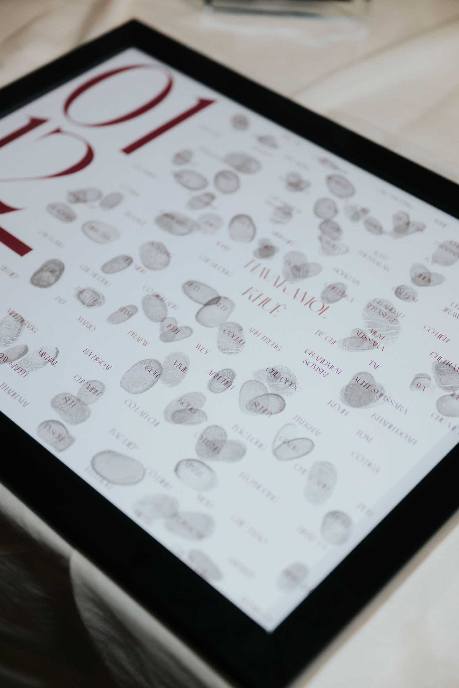 Framed fingerprint guest book with red numbers and signatures, a unique wedding keepsake displayed on a white surface.