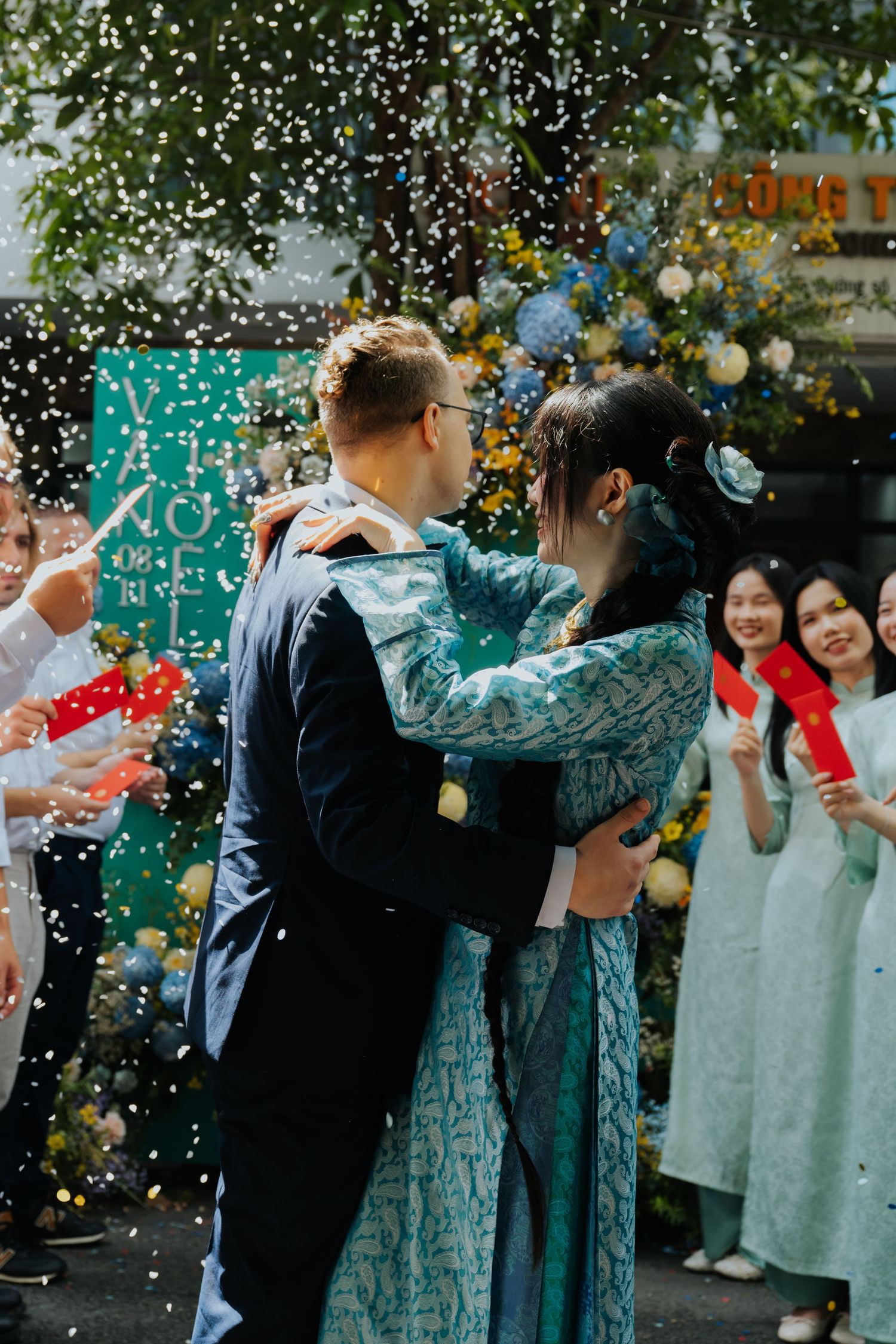 A couple shares a romantic embrace during a wedding ceremony with confetti falling and guests celebrating around them.