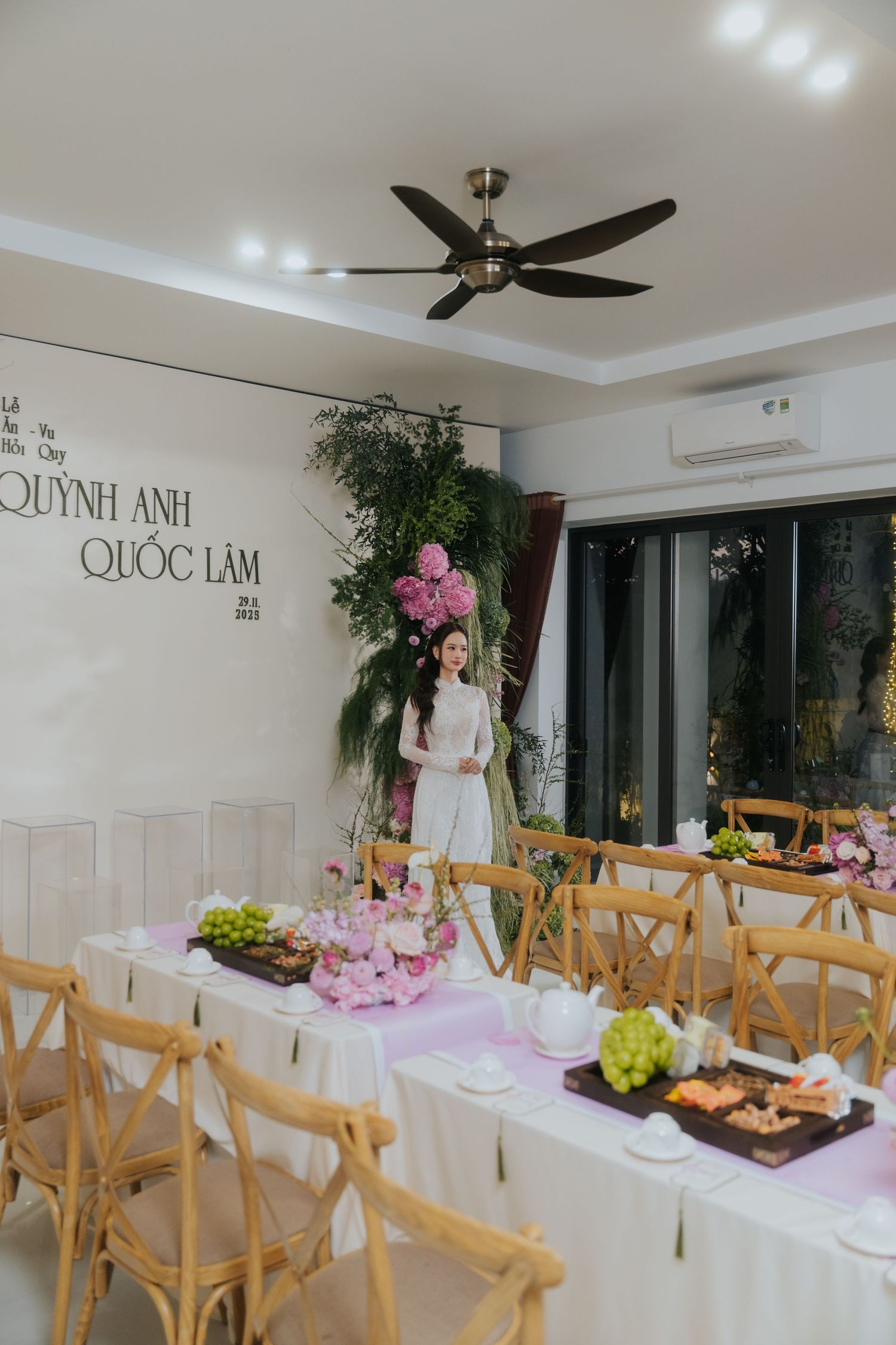 Elegant Vietnamese wedding venue with wooden chairs, floral arrangements, and names Quynh Anh & Quoc Lam displayed on wall.