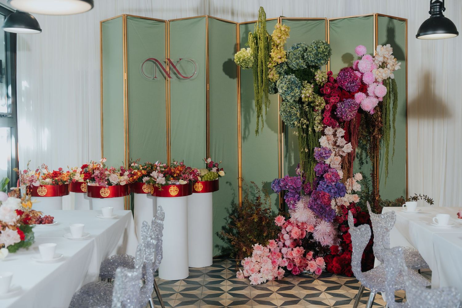 Elegant floral wedding display with colorful blooms on white pedestals and a decorative green folding screen backdrop.