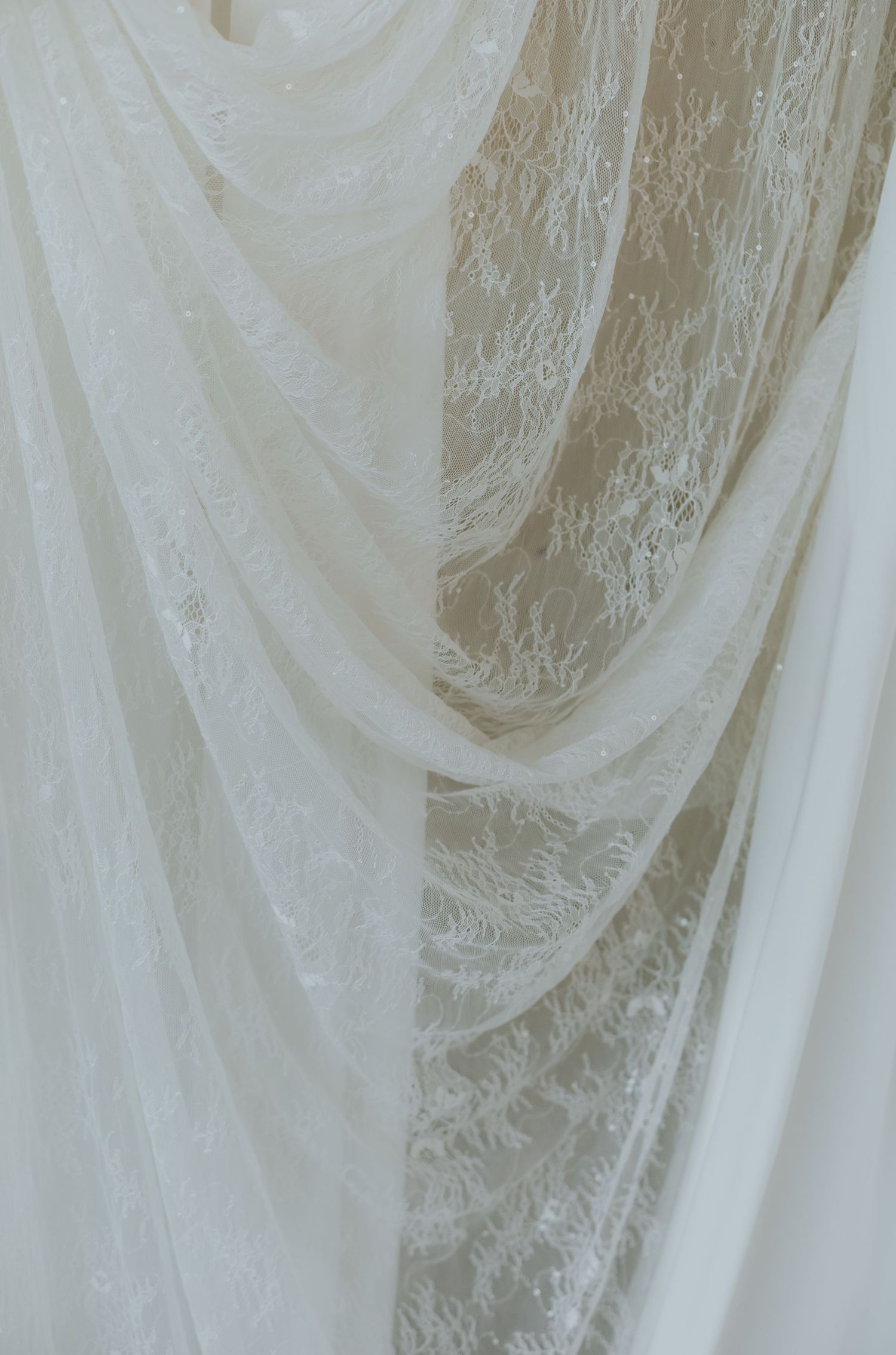 Elegant white lace and tulle fabric draped gracefully, featuring delicate floral patterns, perfect for bridal or formal wear.