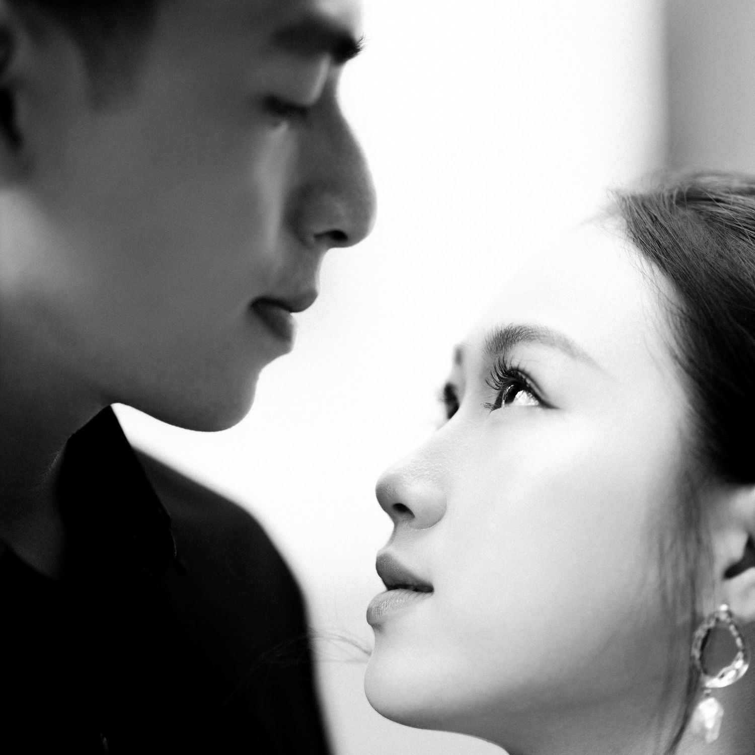 Black and white close-up portrait of a man and woman facing each other intimately, woman wearing elegant drop earrings.