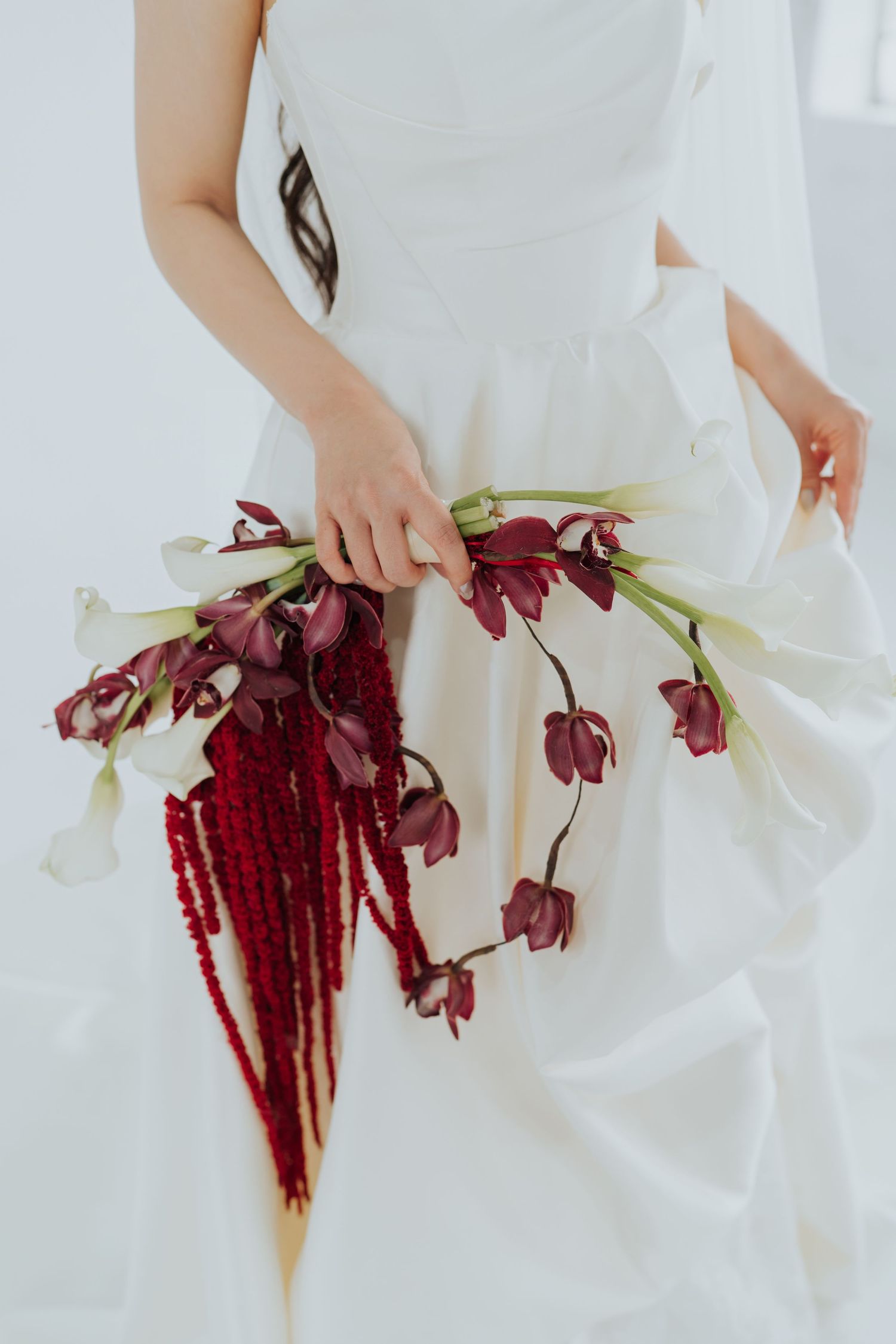 Bride in white gown holding cascading burgundy and white floral bouquet with amaranthus and tulips.