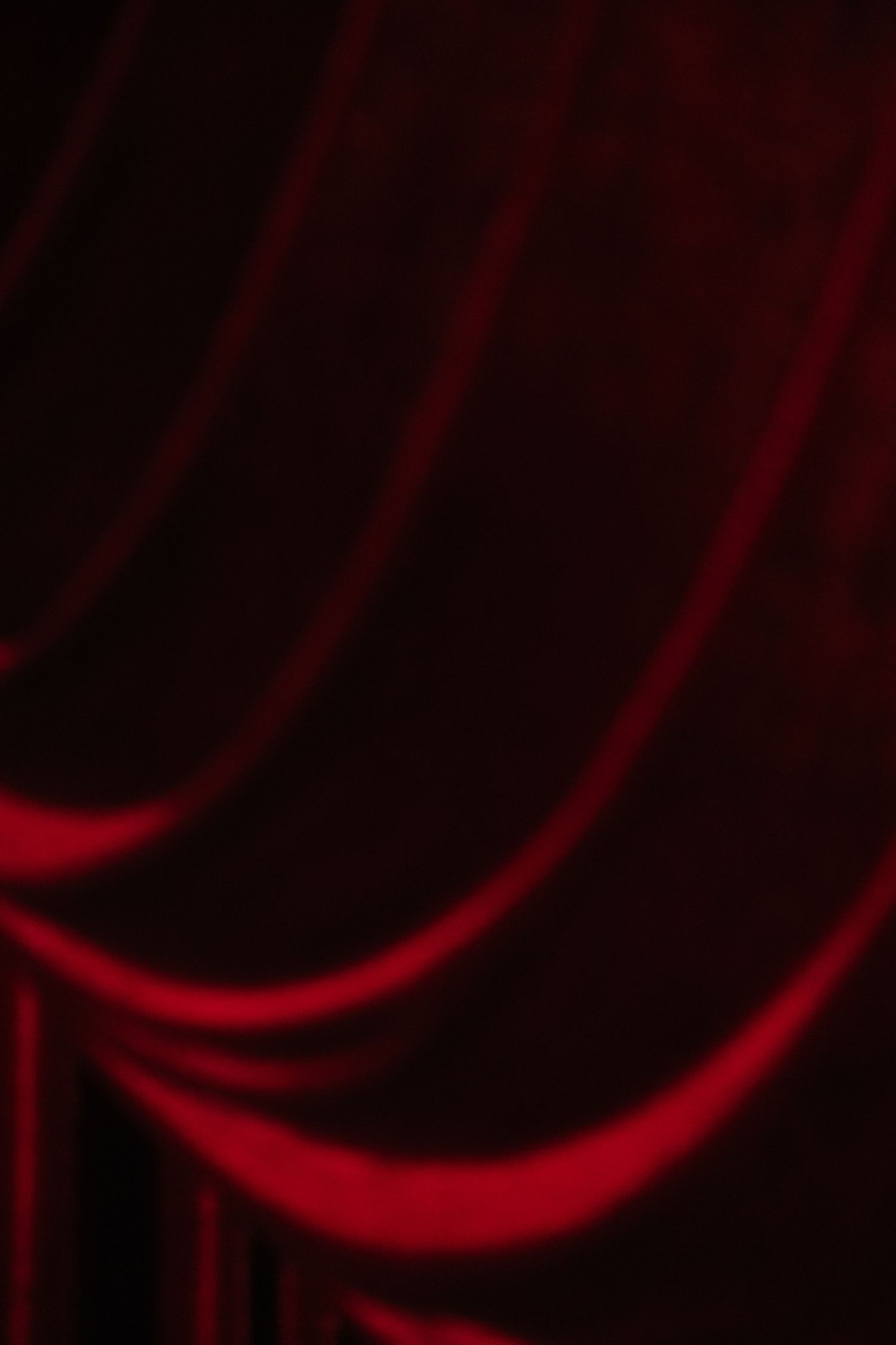 Deep red velvet theater curtains dramatically lit, creating elegant flowing folds and shadows on stage.