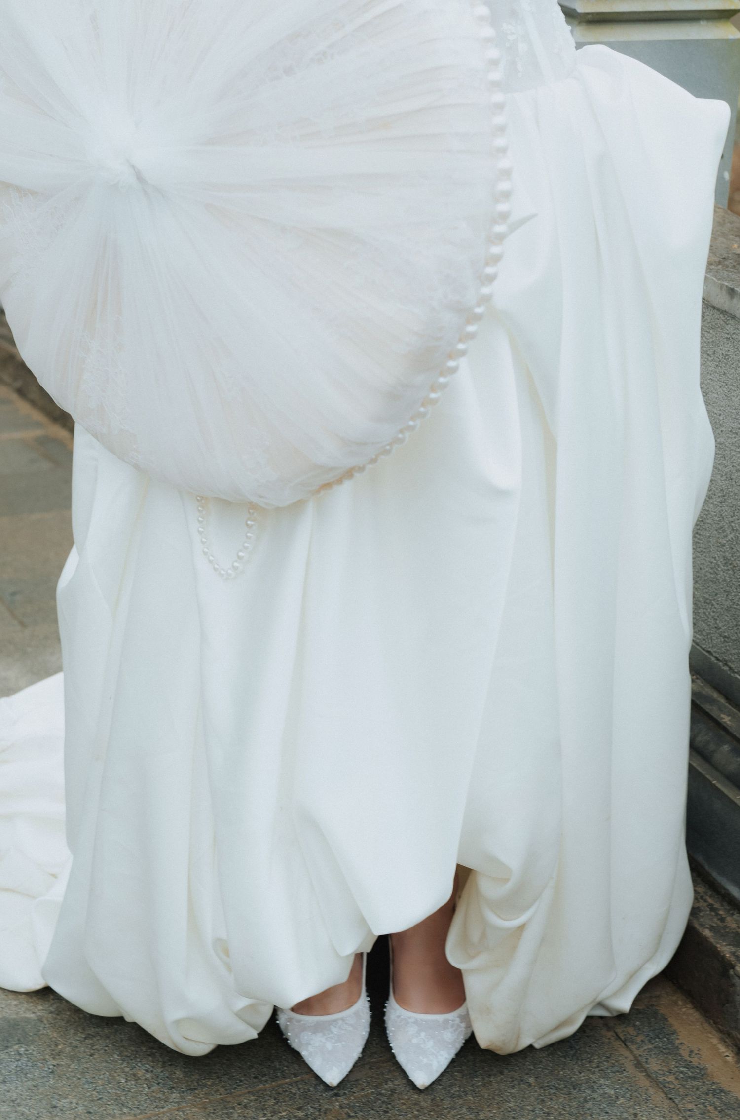 Bride in a white wedding gown with a large bow detail and white pointed-toe heels visible beneath the flowing dress.