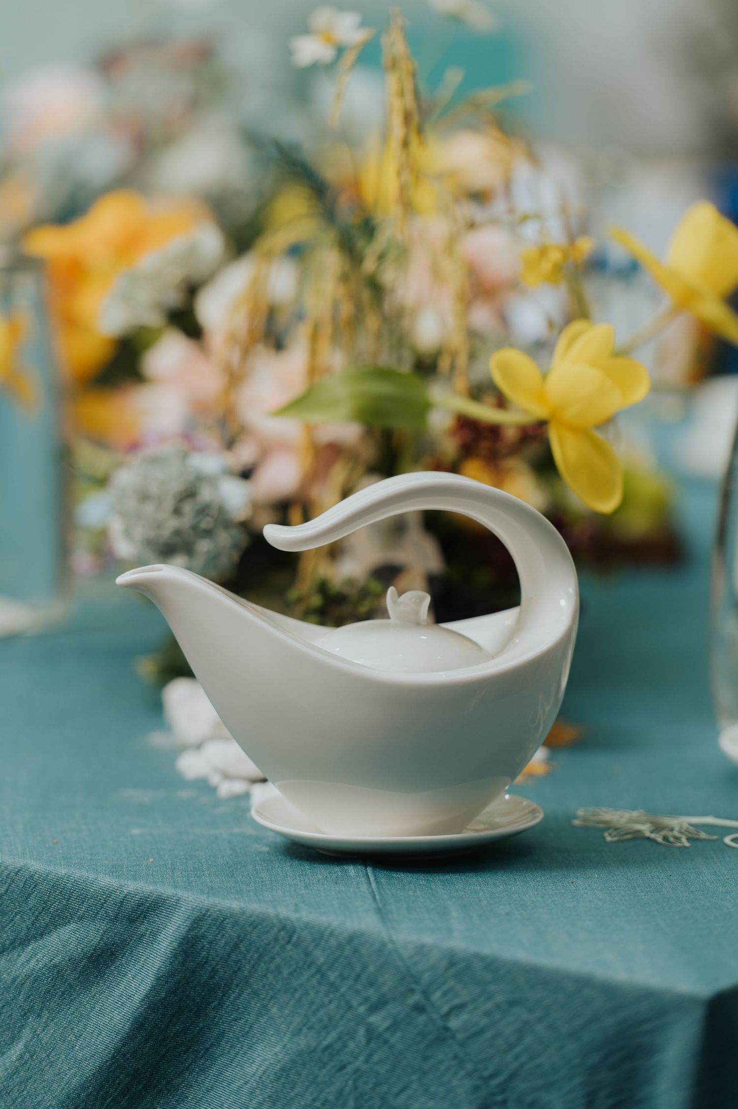 White ceramic gravy boat on teal linen tablecloth with colorful spring floral arrangement in background.