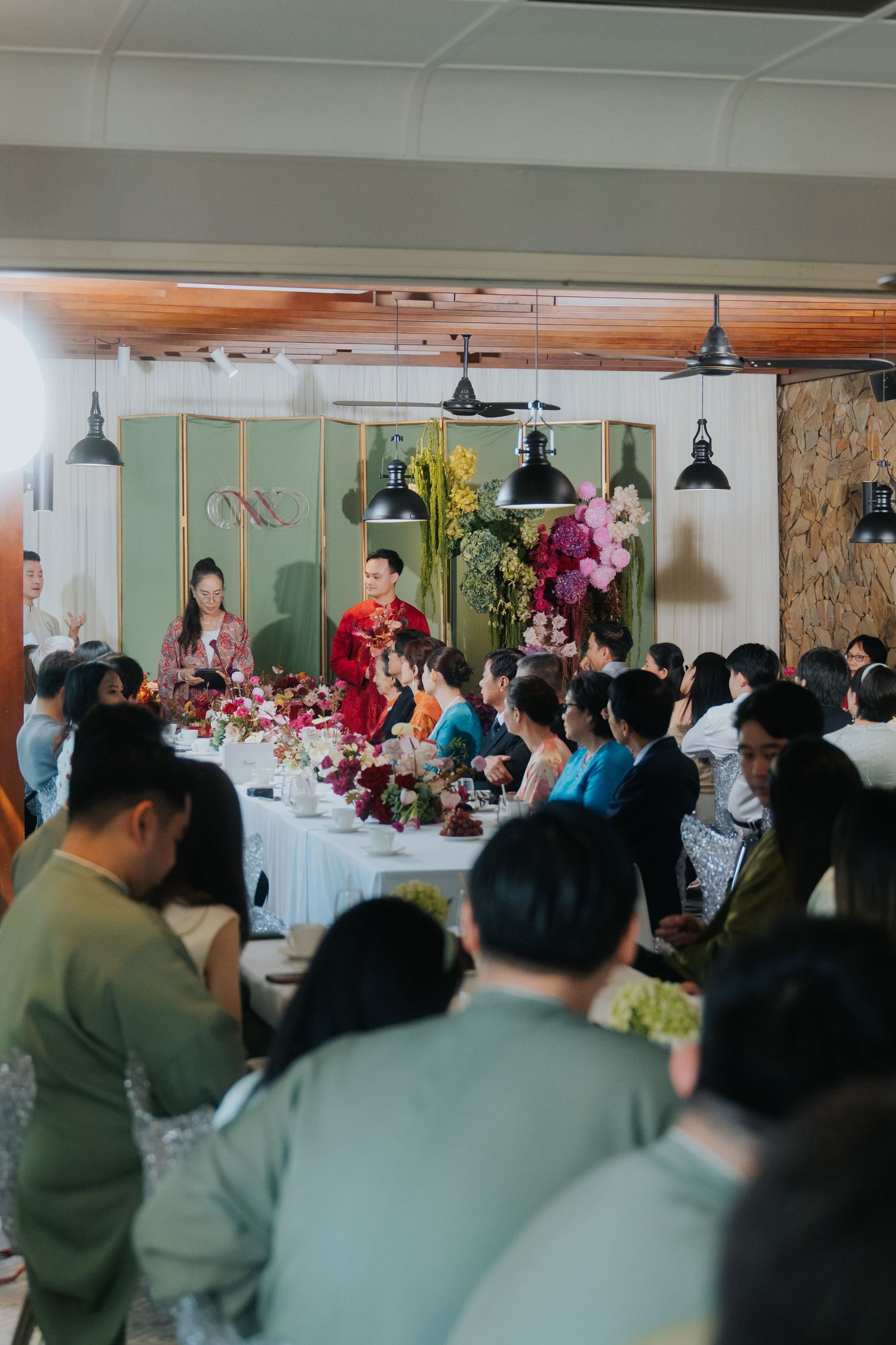 Elegant wedding reception with guests seated at long tables, couple in traditional red attire at the head table with floral decor.