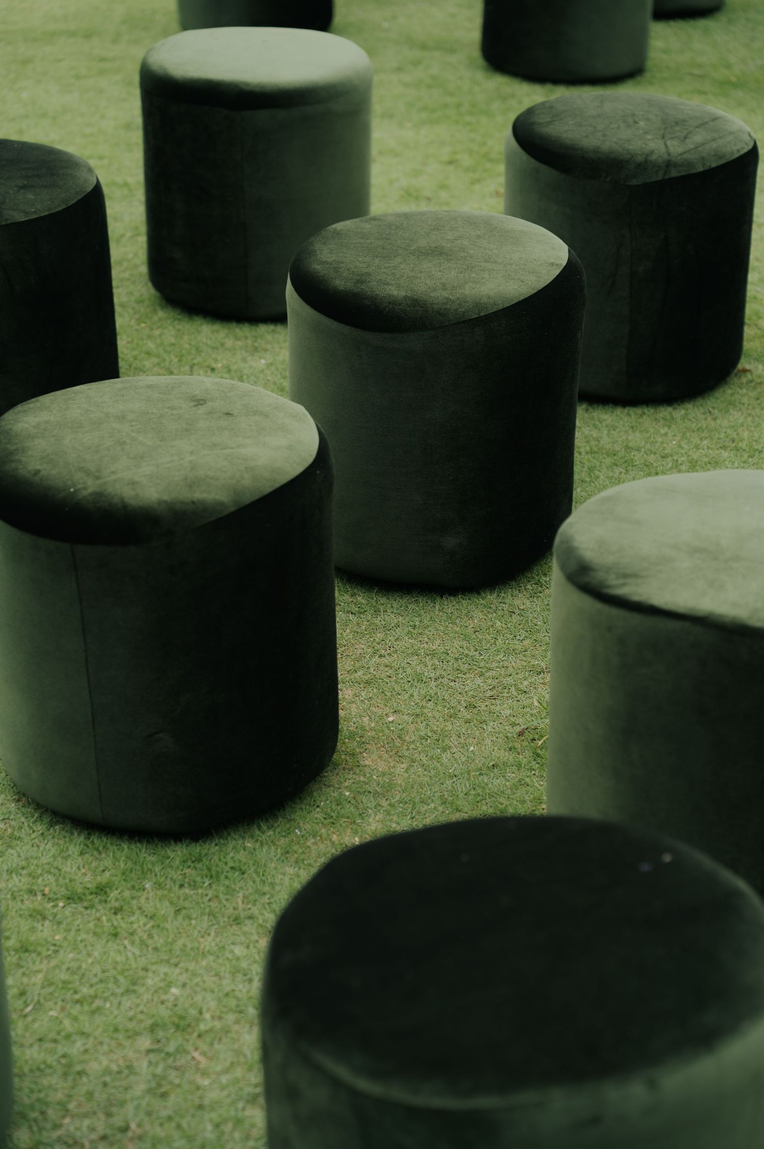 Dark green velvet cylindrical ottomans arranged on lush grass lawn for outdoor seating event.