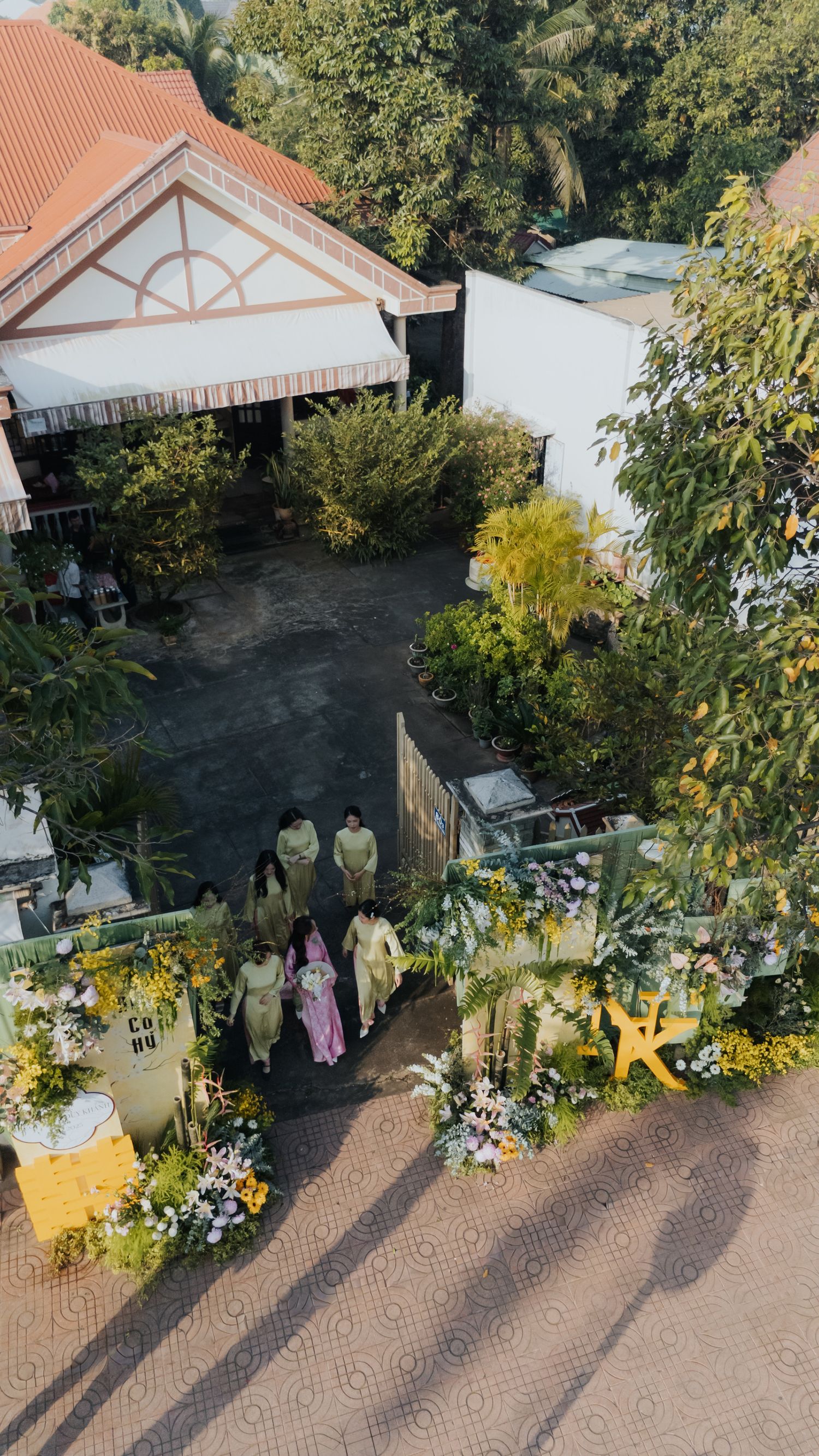Aerial view of a Vietnamese wedding ceremony entrance decorated with yellow flowers and greenery outside a traditional house.