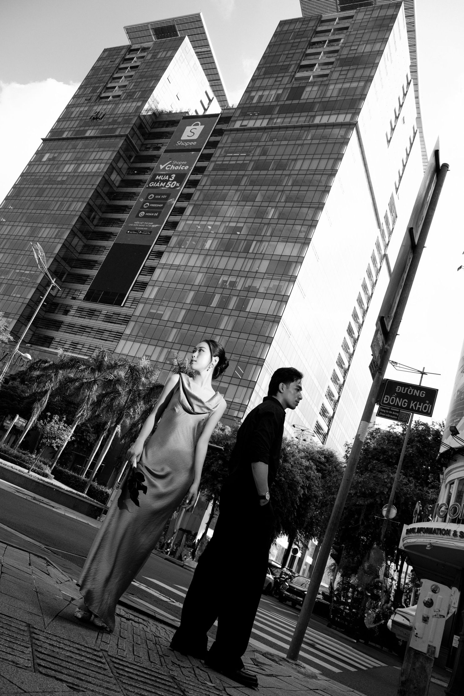 Black and white photo of a couple standing on a city street with modern glass skyscrapers in the background.