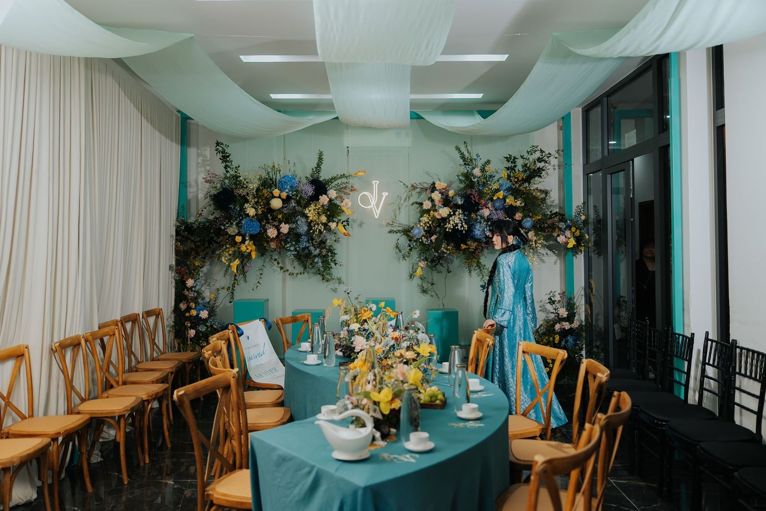 Elegant wedding reception with teal tablecloths, wooden cross-back chairs, and lush floral arrangements in blue and yellow tones.