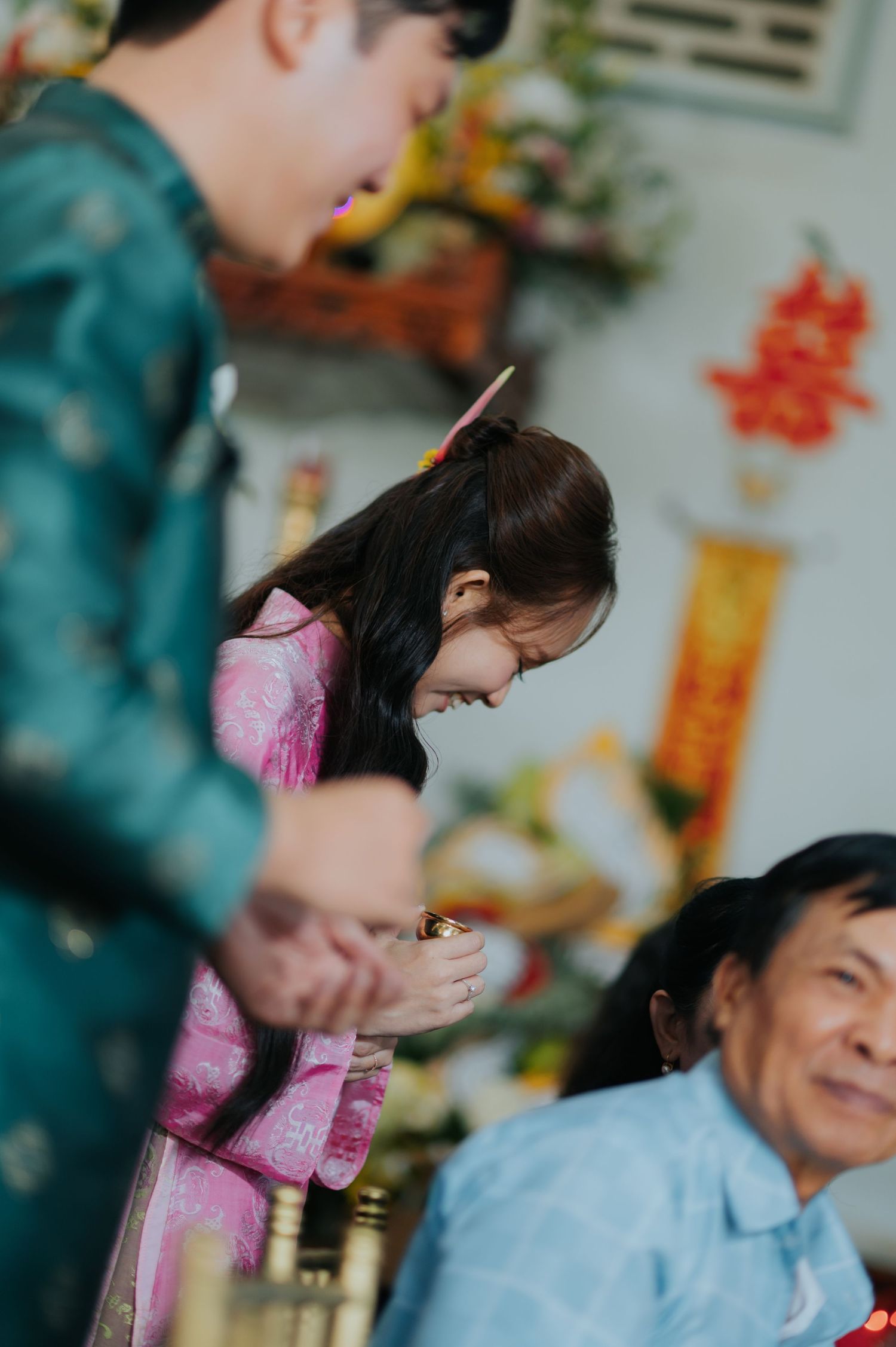 Young girl in pink ao dai bowing respectfully during a Vietnamese traditional ceremony with elders present.