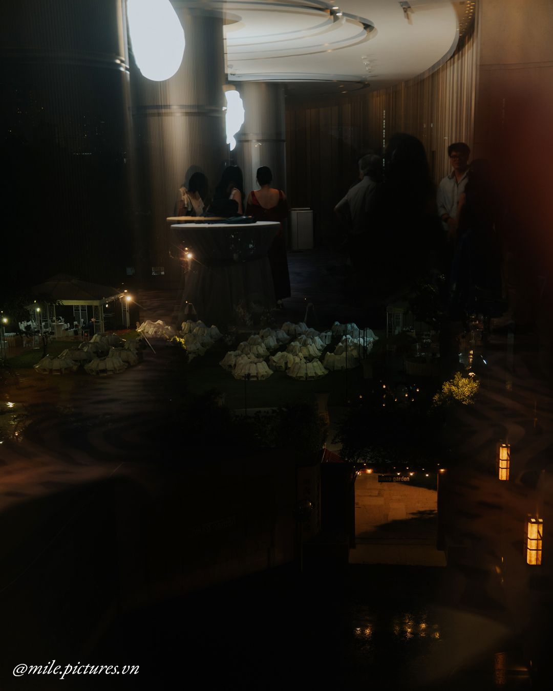 Dimly lit elegant event space with floral arrangements, candles, and guests mingling near a bar.