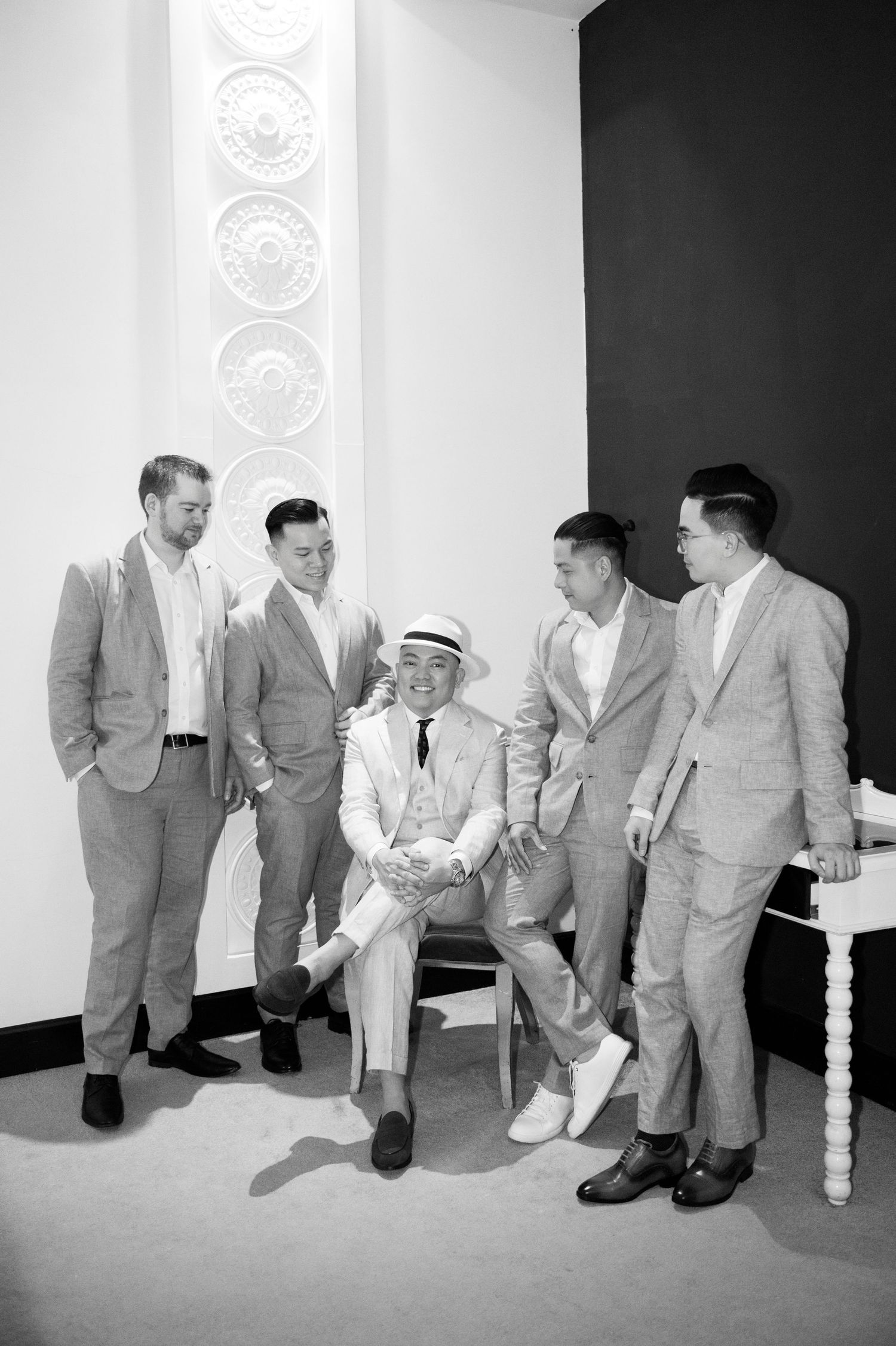 Black and white photo of five men in suits laughing together, one seated wearing a panama hat and tie.