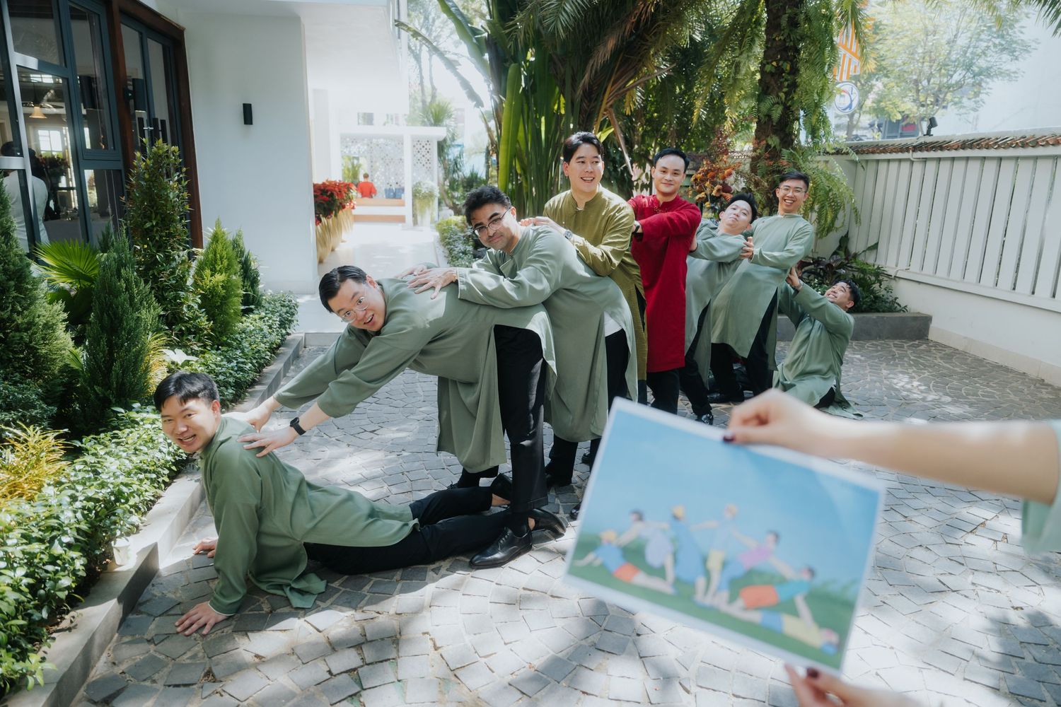 Group of friends in matching green outfits posing playfully outdoors near a white building with tropical plants.