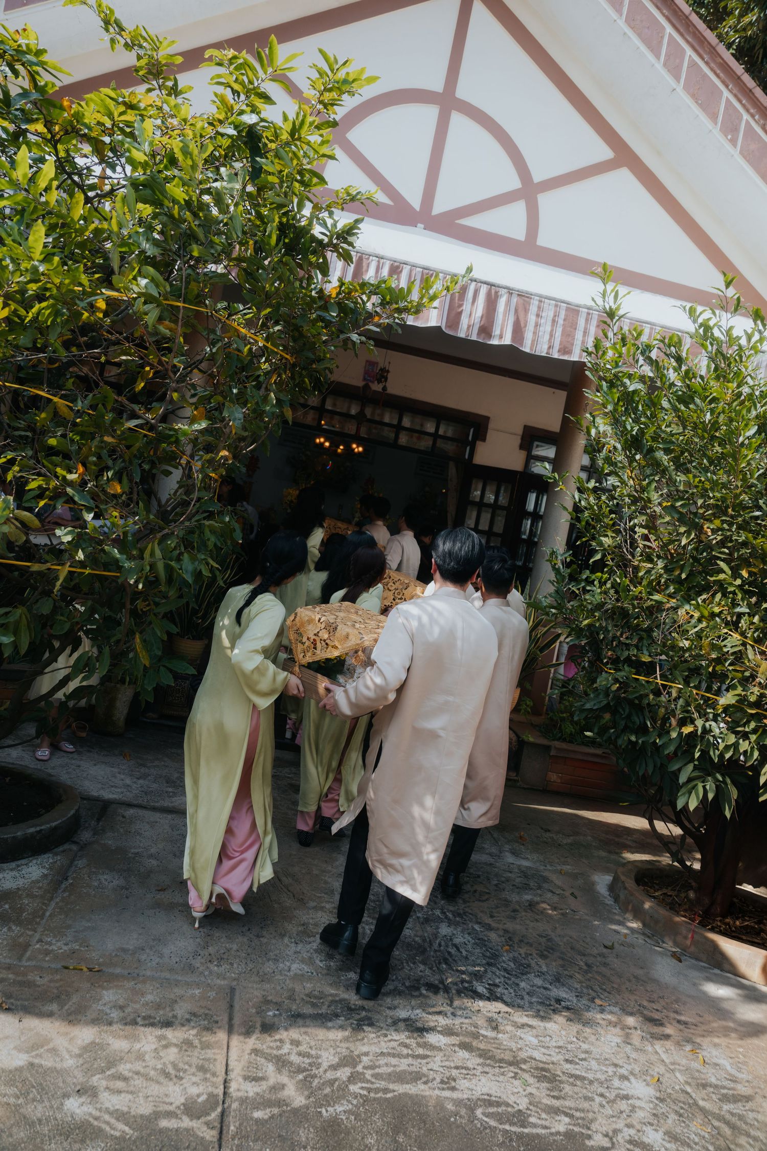 People in traditional Vietnamese ao dai attire entering a home during a ceremonial gathering.