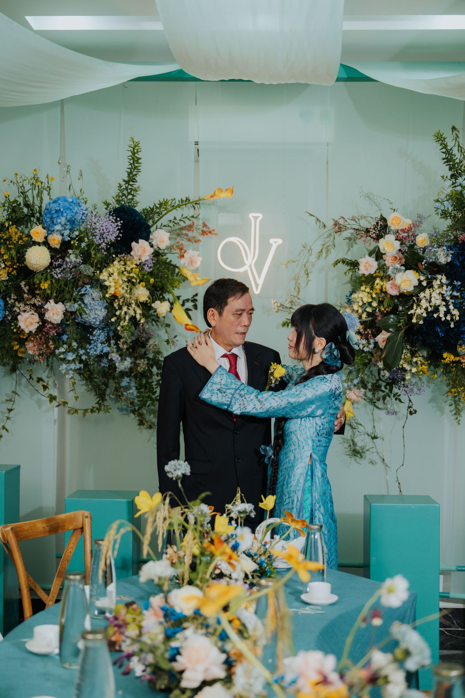 Couple sharing a tender moment at a teal-themed wedding reception with floral arch backdrop and yellow blooms.