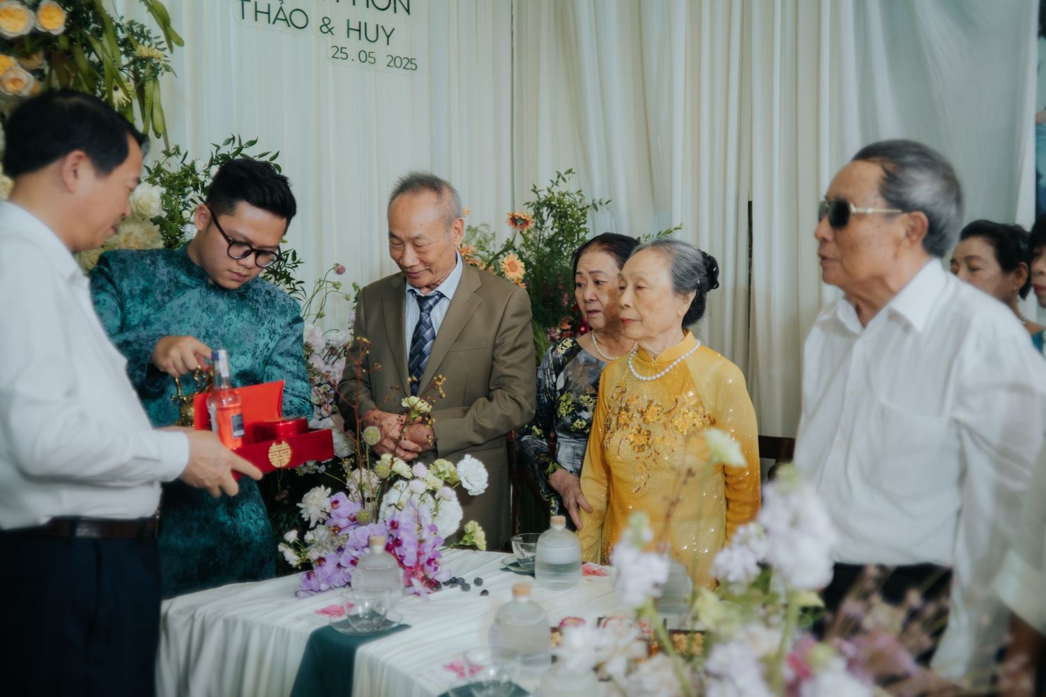 Guests gather around a decorated table at a Vietnamese wedding reception for Thao and Huy, exchanging gifts and flowers.