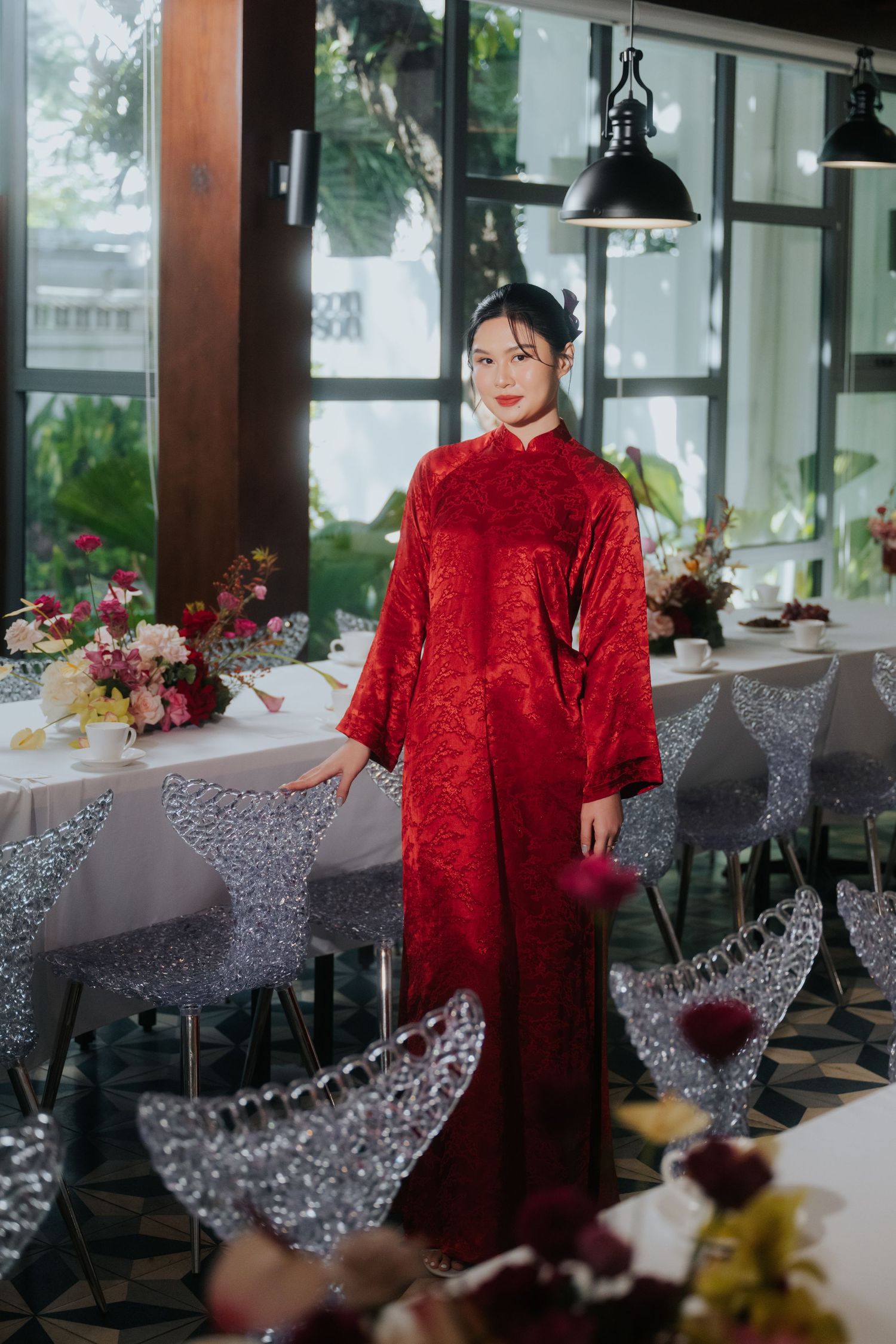 Young woman in elegant red Vietnamese ao dai dress poses gracefully in a decorated restaurant setting.