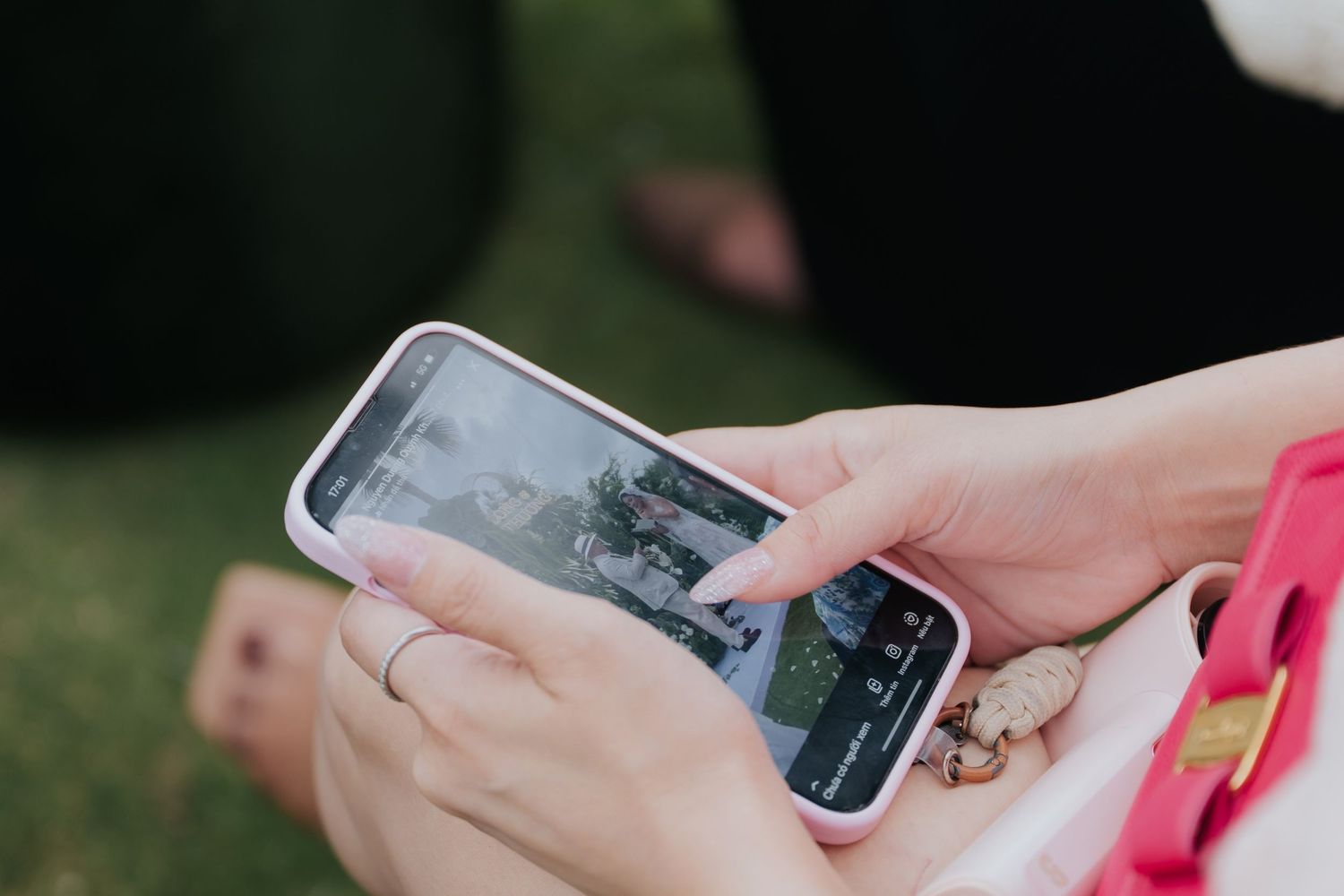 Close-up of hands holding a white smartphone with a pink case, viewing photos outdoors.