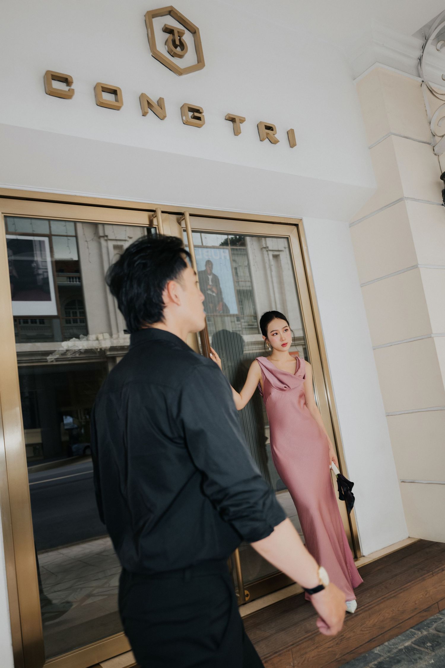 A man in black holds a door for a woman in a pink satin dress at the Constri building entrance.