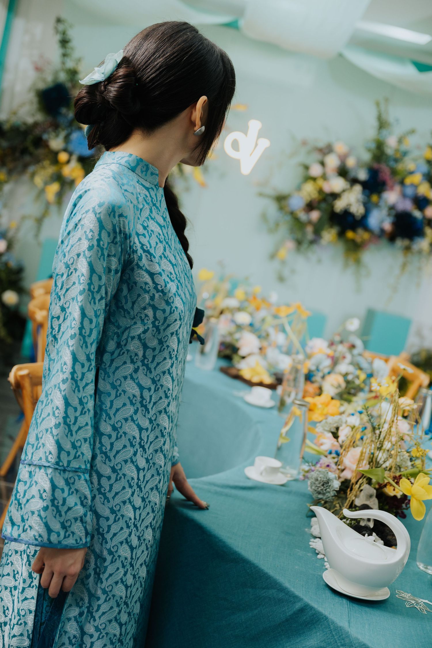 Woman in blue patterned dress admiring floral table decorations at an elegant event.