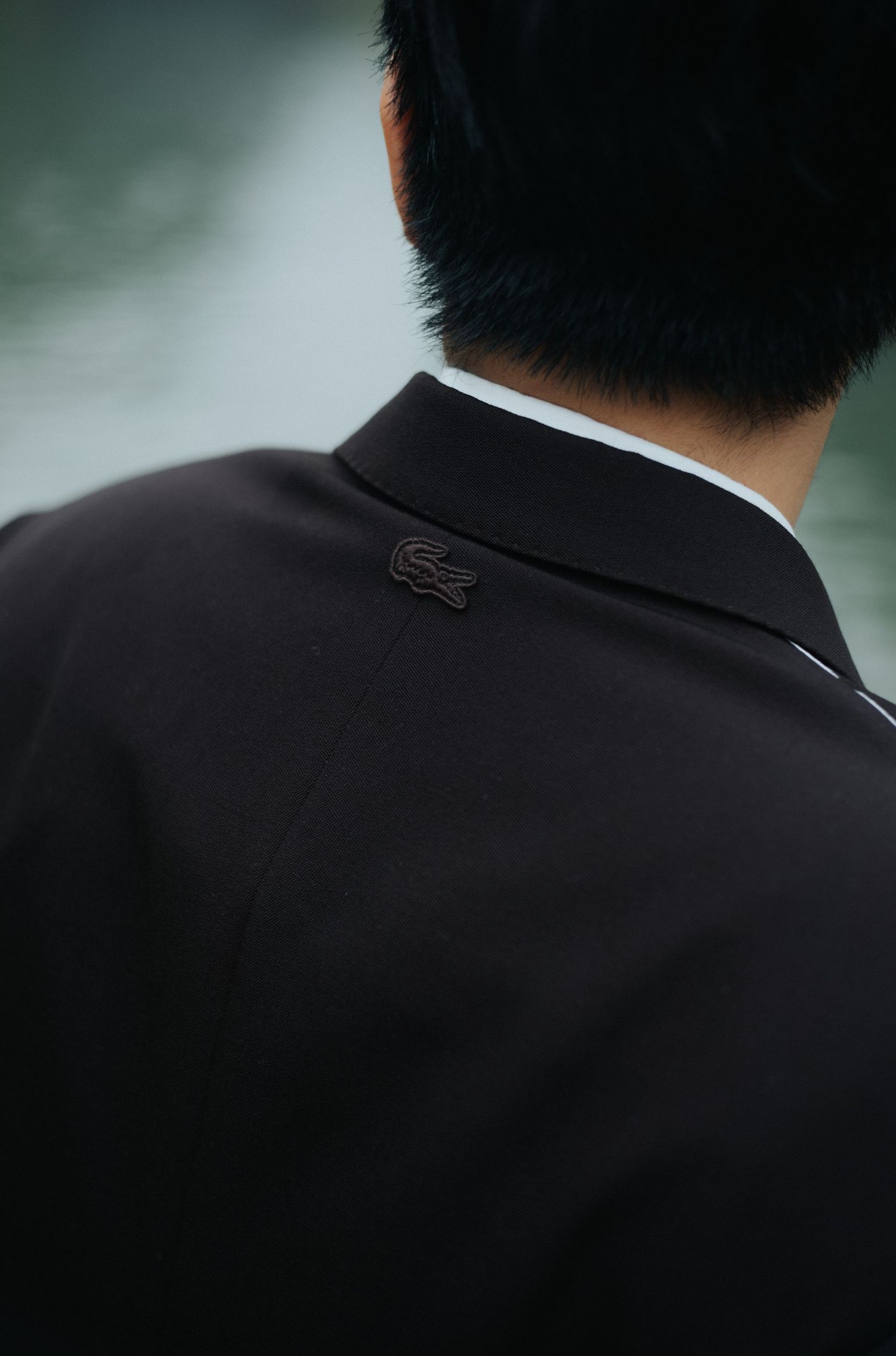 Close-up of a man wearing a dark Lacoste polo shirt, showcasing the iconic crocodile logo on the chest.