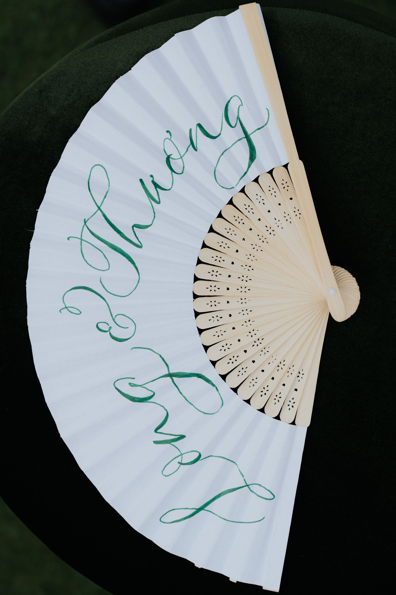 White hand fan with green Vietnamese calligraphy script, featuring decorative wooden ribs and elegant cursive lettering.