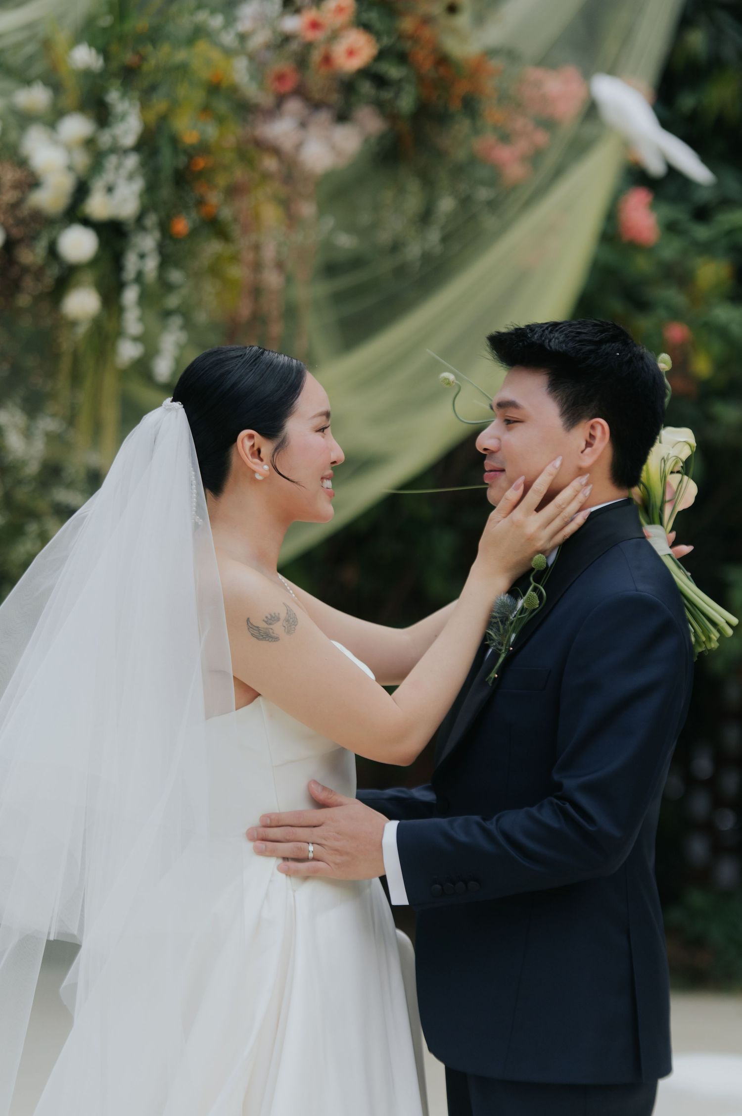 A bride and groom share a tender moment at their outdoor wedding ceremony, surrounded by floral arrangements.