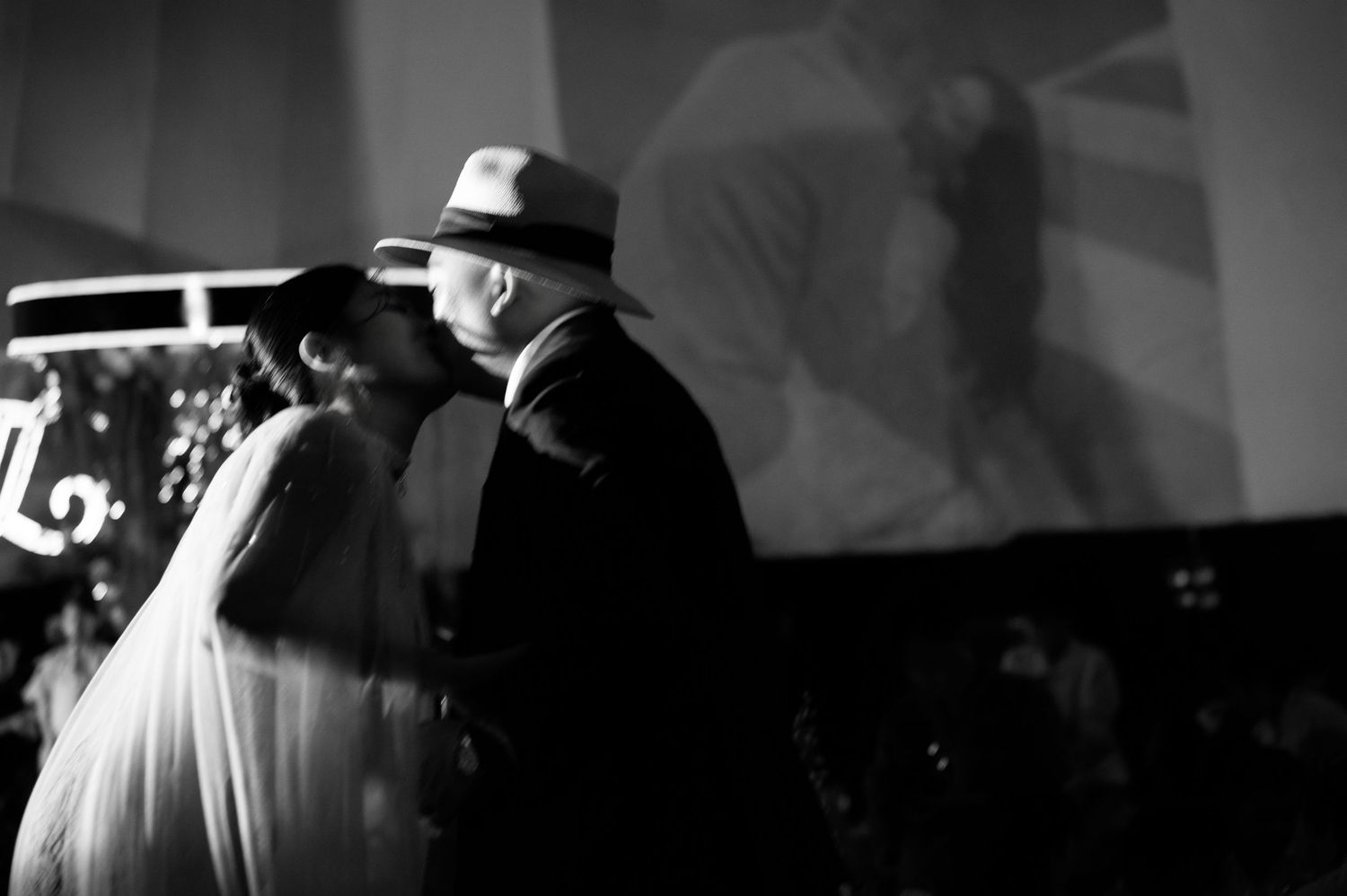 Black and white photo of a bride and groom in fedora hats sharing an intimate moment at their wedding reception.