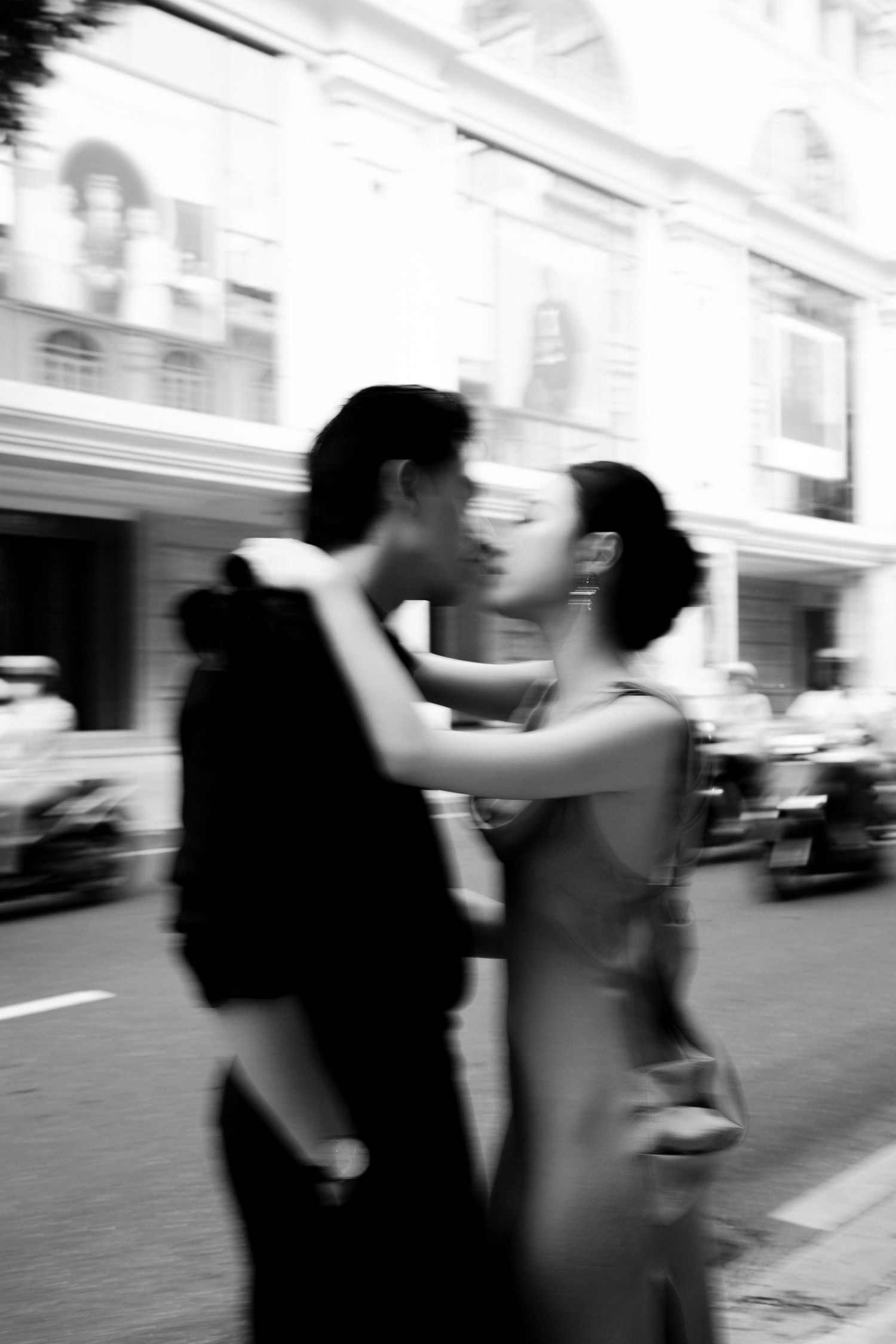 Black and white photo of a couple sharing a romantic moment on a city street, motion blur adding artistic effect.