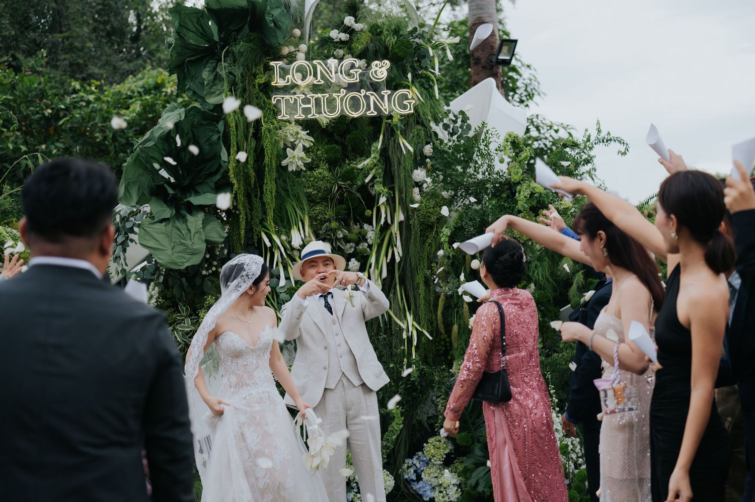 Bride and groom walk down the aisle at an outdoor wedding ceremony with lush green floral arch backdrop.