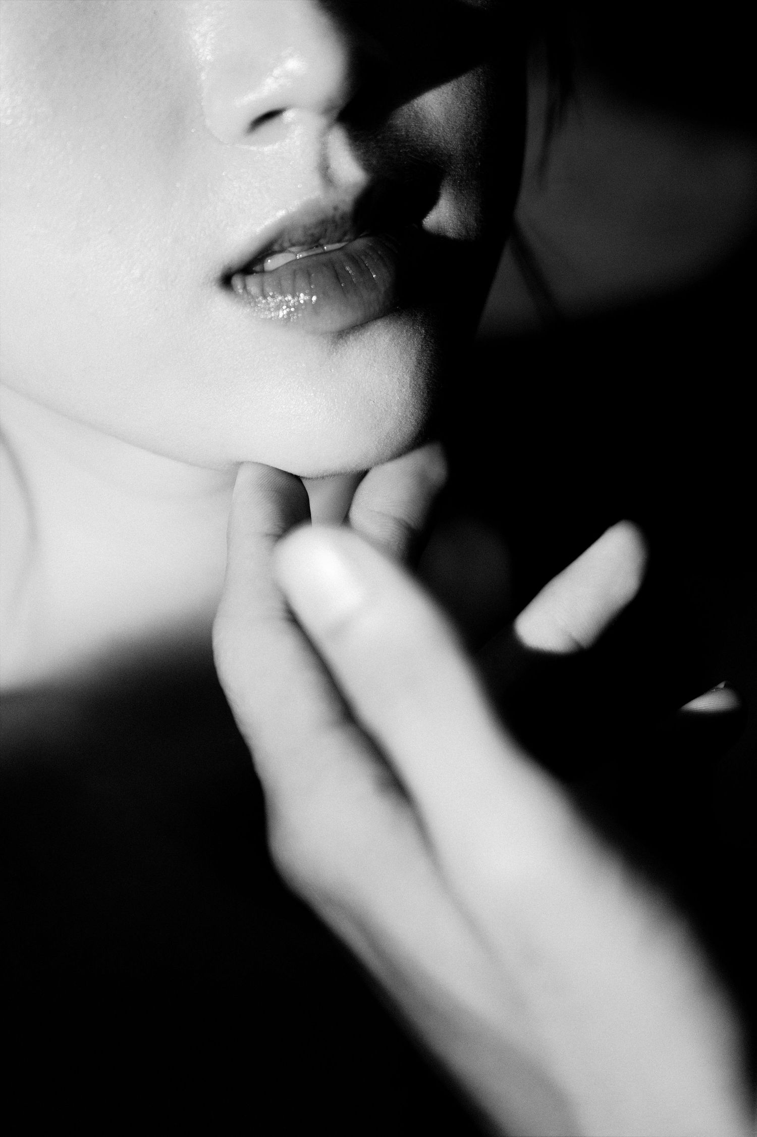 Black and white close-up of glossy lips with a hand gently touching the chin in an artistic portrait.