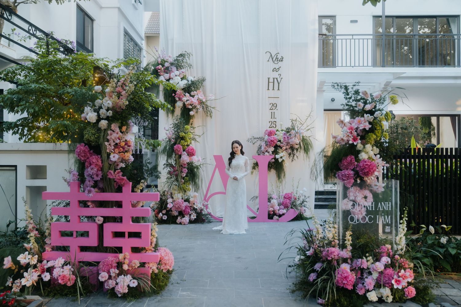 Elegant outdoor wedding venue decorated with pink floral arrangements and a bride standing in white dress.
