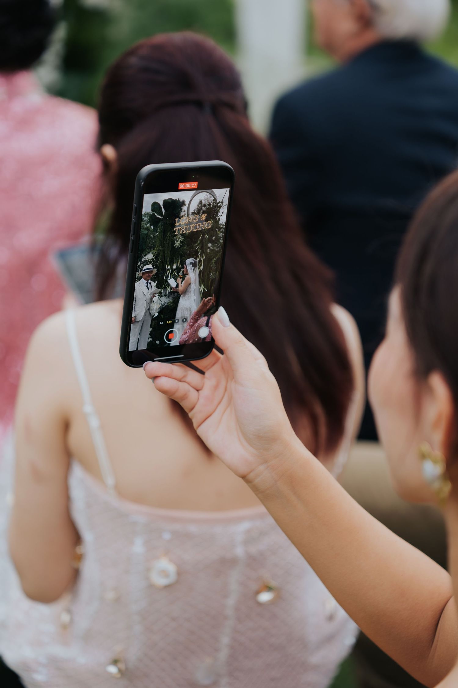 Guest recording a wedding ceremony on a smartphone, capturing the bride and groom at an outdoor celebration.