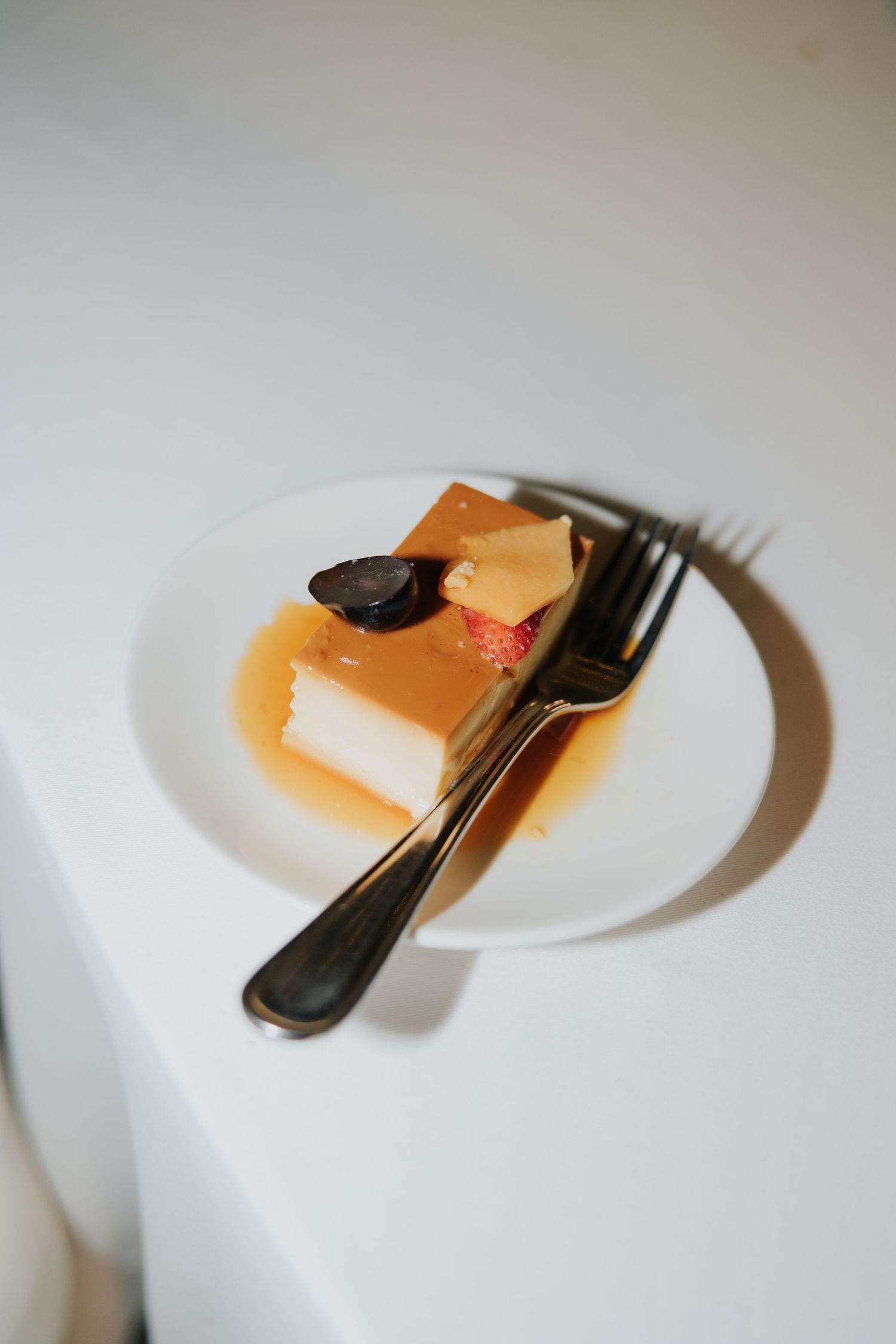 A slice of layered caramel cake with strawberry and chocolate garnish on a white plate with a fork.