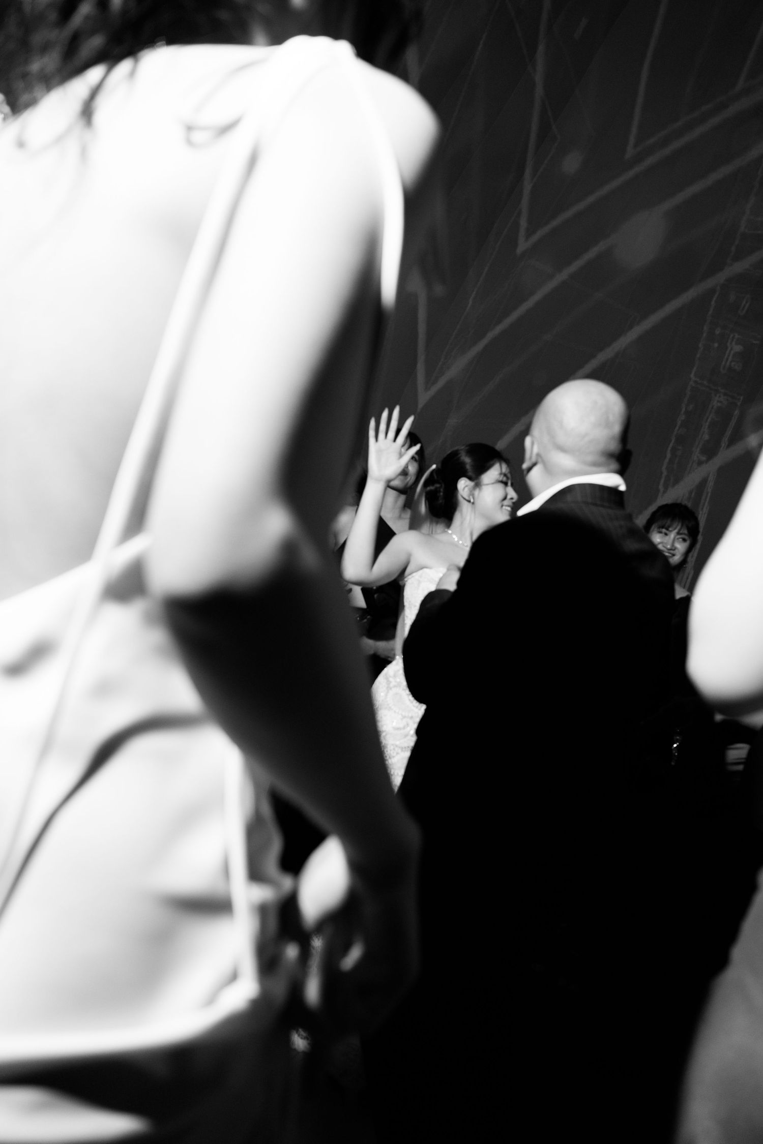 Black and white wedding photo of bride and groom sharing first dance while guests watch in elegant venue.