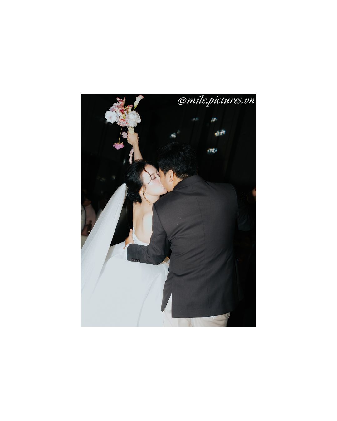 A couple shares a romantic kiss at their wedding, bride holding a floral bouquet, groom in dark suit.