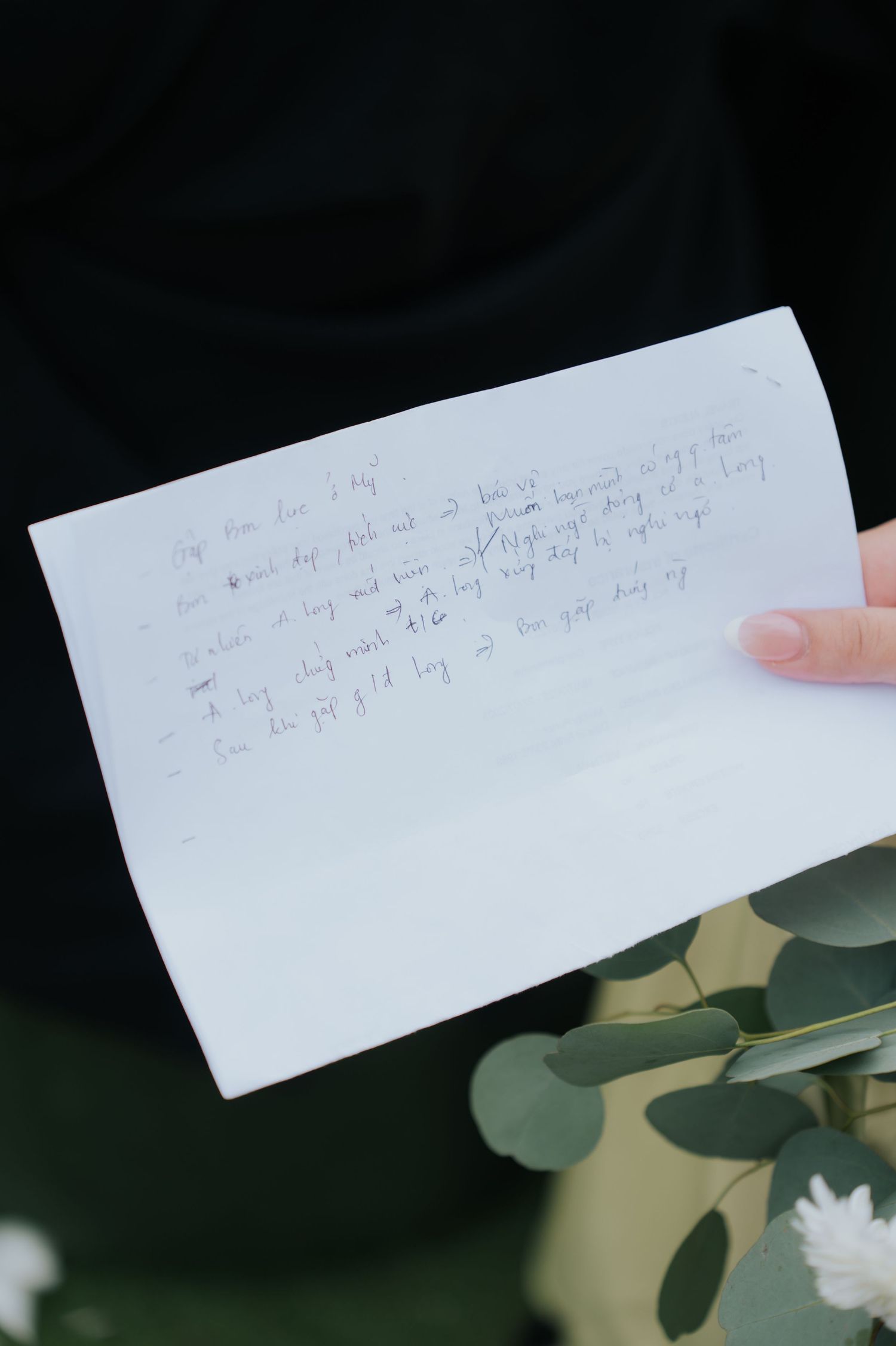 Hand holding a handwritten note on white paper with green eucalyptus leaves in the foreground.