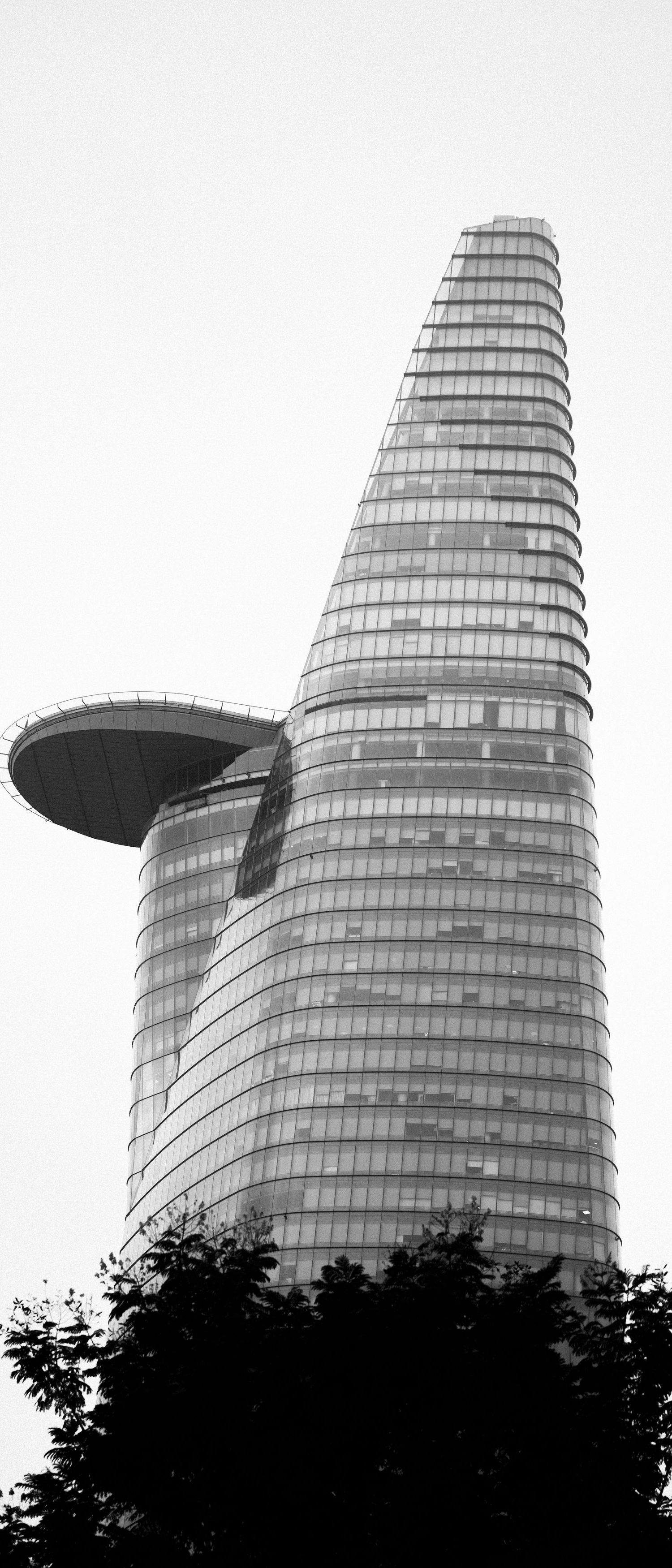 Black and white photo of a modern skyscraper with unique curved architecture against a clear sky.