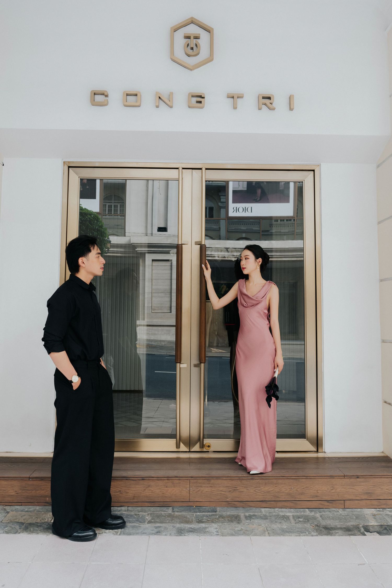 A man in black and woman in pink satin gown pose outside the Cong Tri fashion boutique entrance.