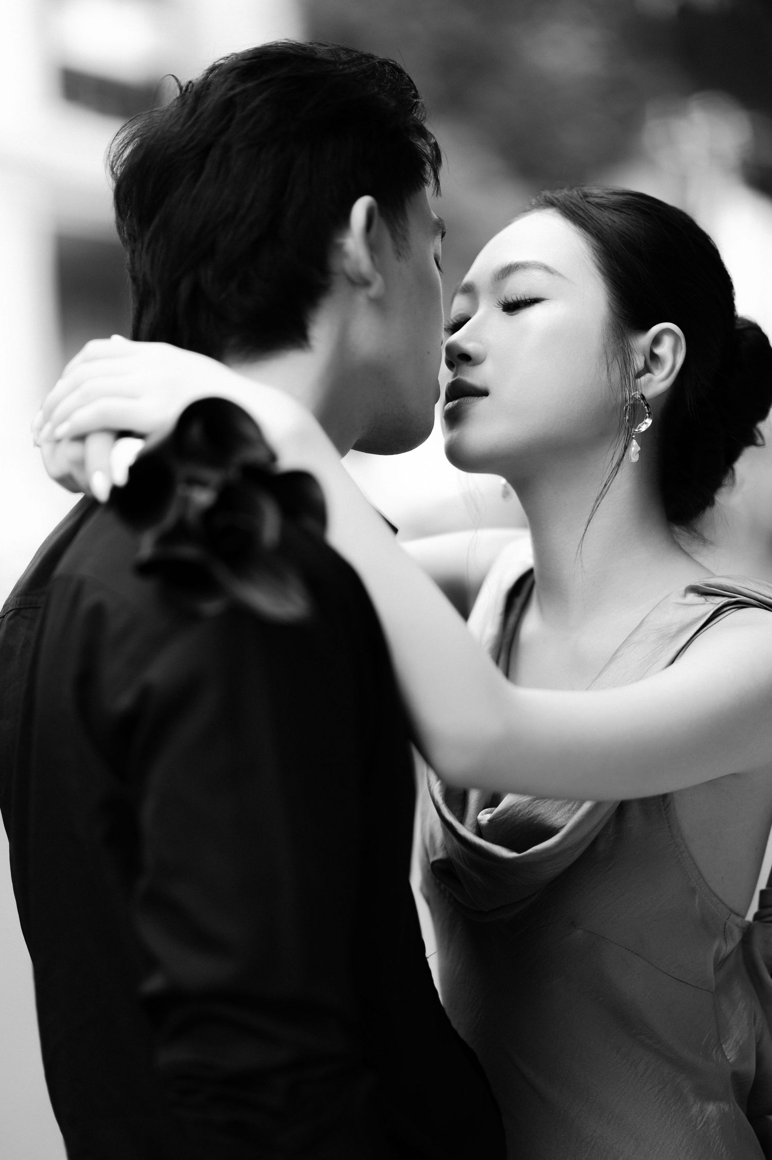 Black and white photo of a couple sharing a romantic moment, woman in elegant dress embracing man in suit.