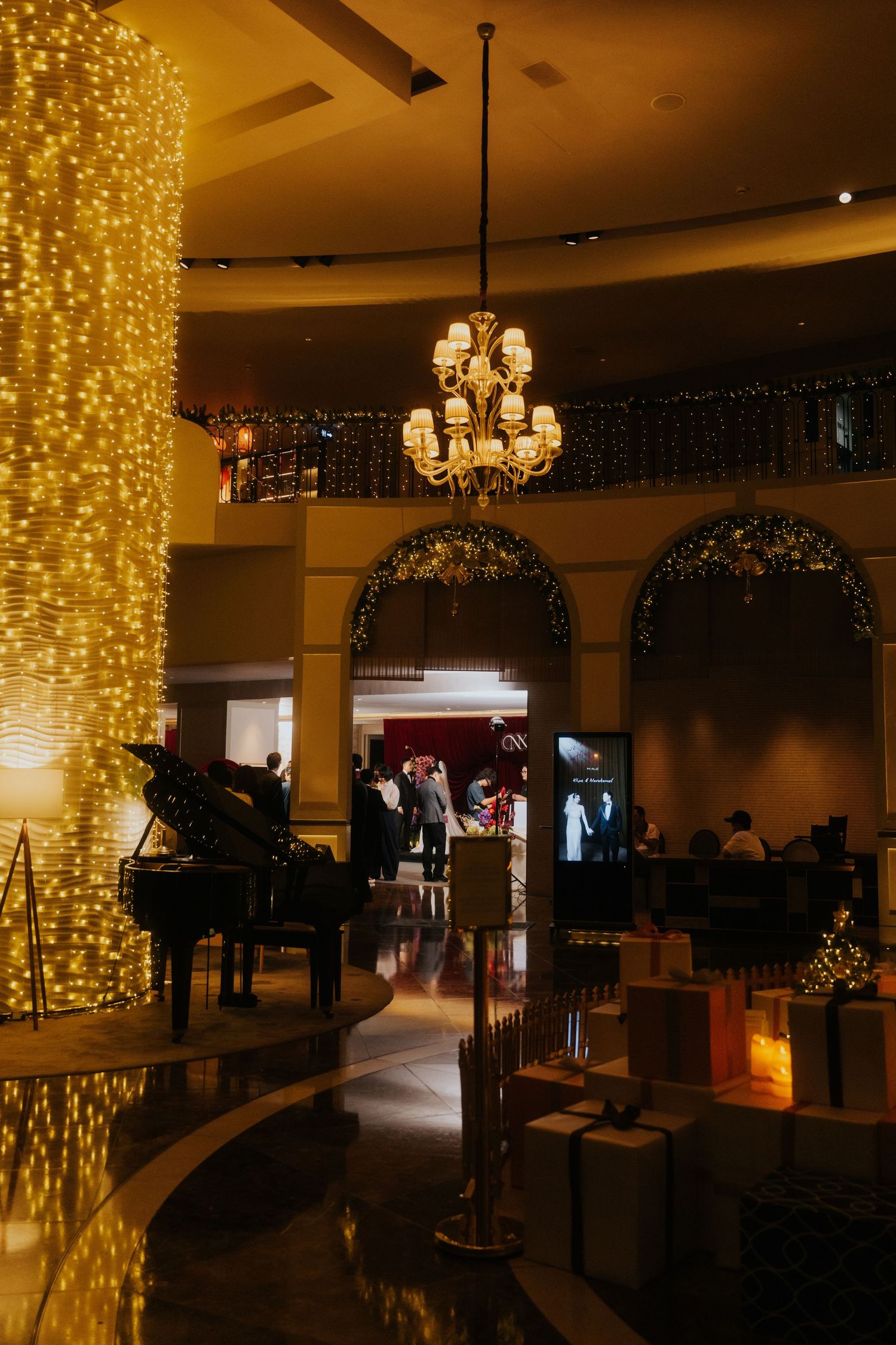 Elegant hotel lobby adorned with golden fairy lights, grand piano, chandelier, and festive Christmas decorations.